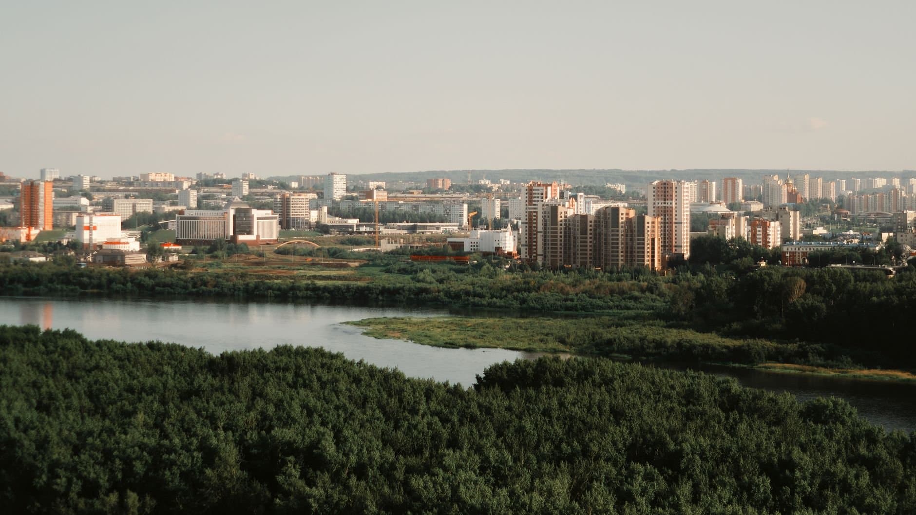 Aerial view of a modern city skyline with river and lush greenery in summer.