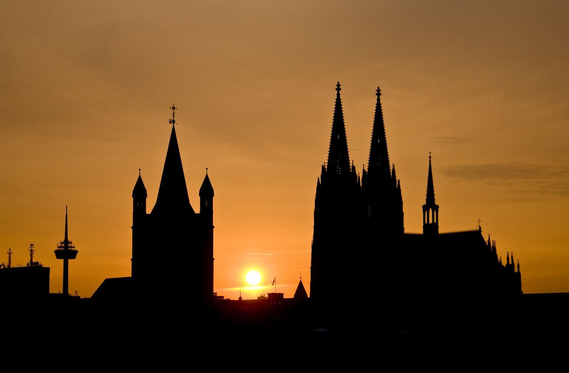 Majestic silhouette of Cologne Cathedral against a vibrant sunset sky.