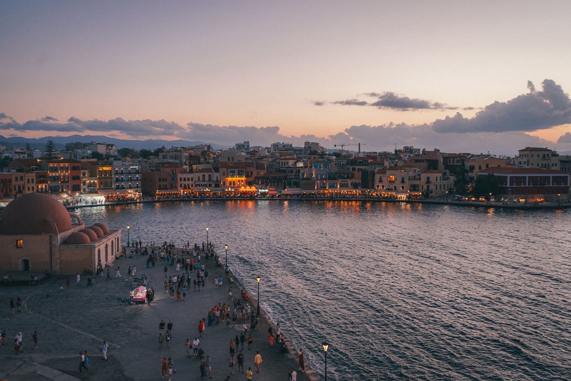 A picturesque sunset view of Chania waterfront in Greece with bustling promenade and tranquil sea.