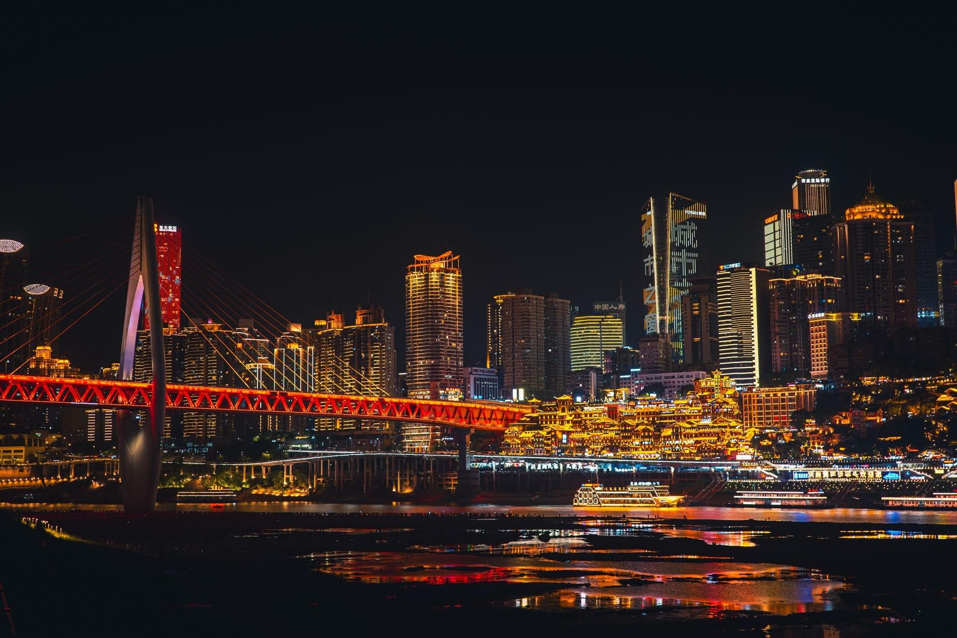 Stunning night view of Chongqing skyline with illuminated bridge over river, showcasing vibrant urban architecture.