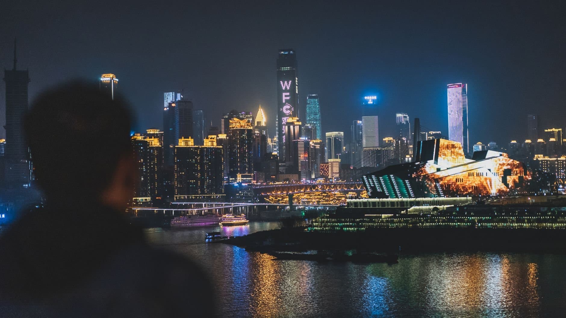 Back view unrecognizable blurred male enjoying amazing view of contemporary illuminated embankment in Chungking China during night