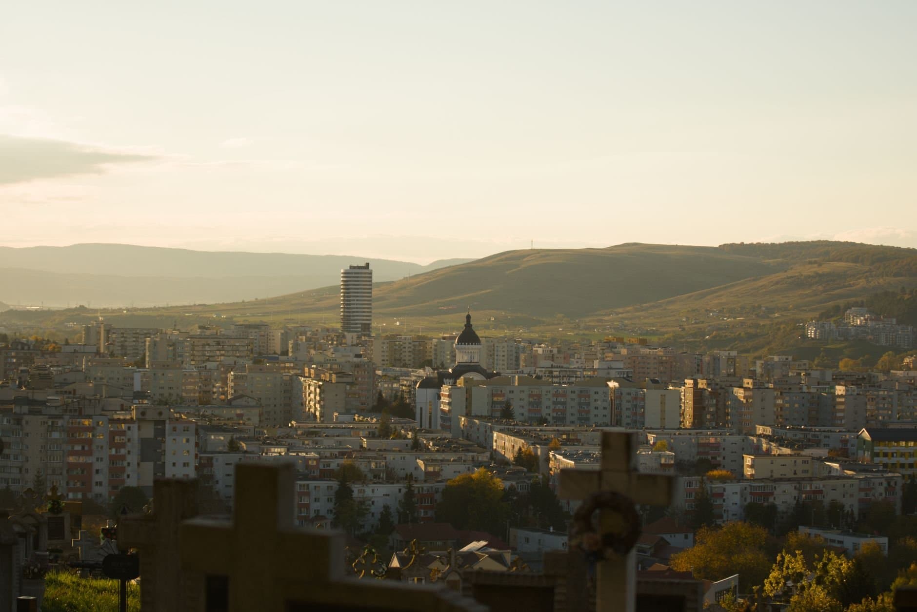 A scenic view of Cluj-Napoca city against the backdrop of rolling hills at sunset.