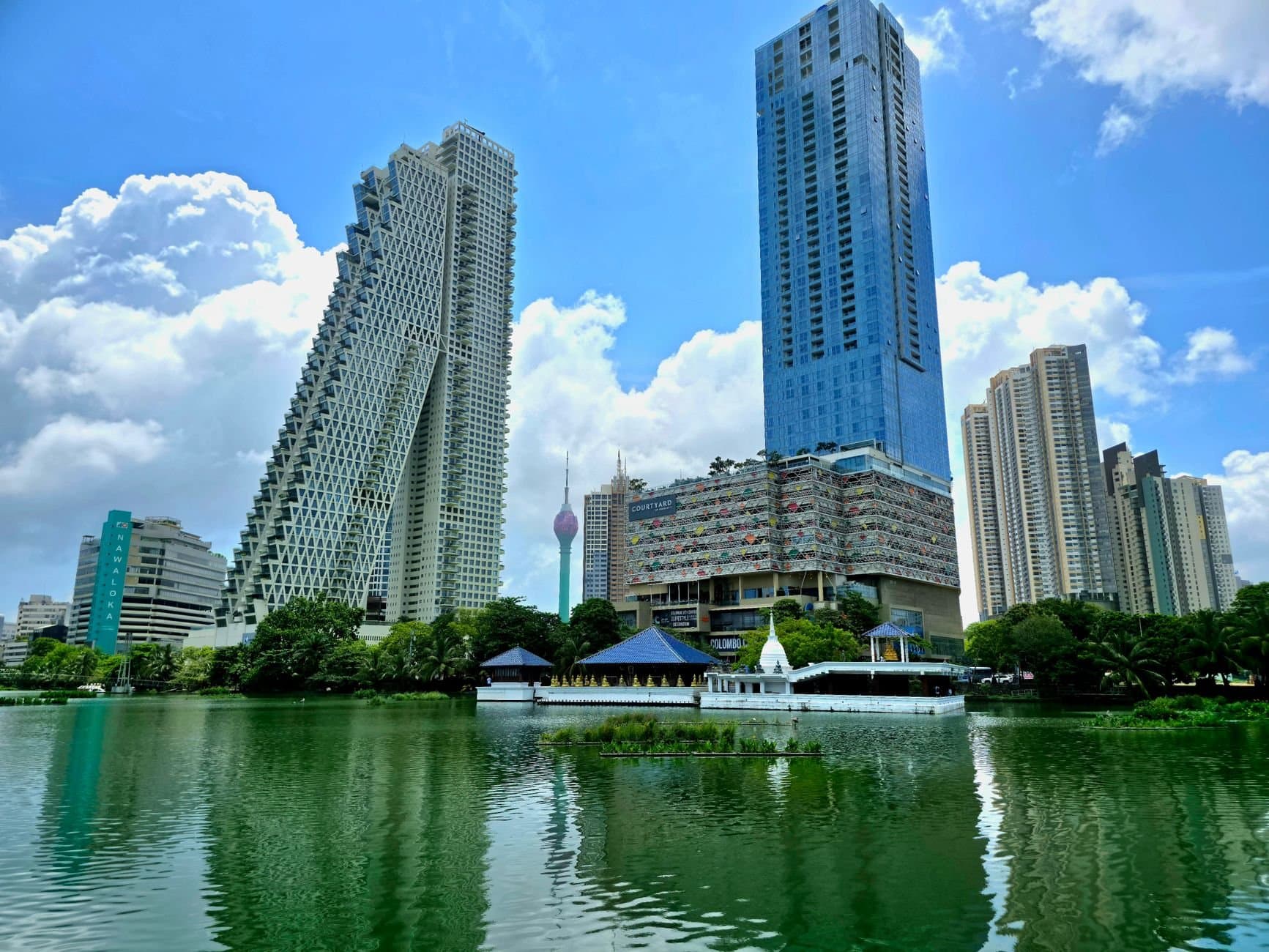 A view of Colombo's skyline with high-rise towers reflecting in a serene lake.