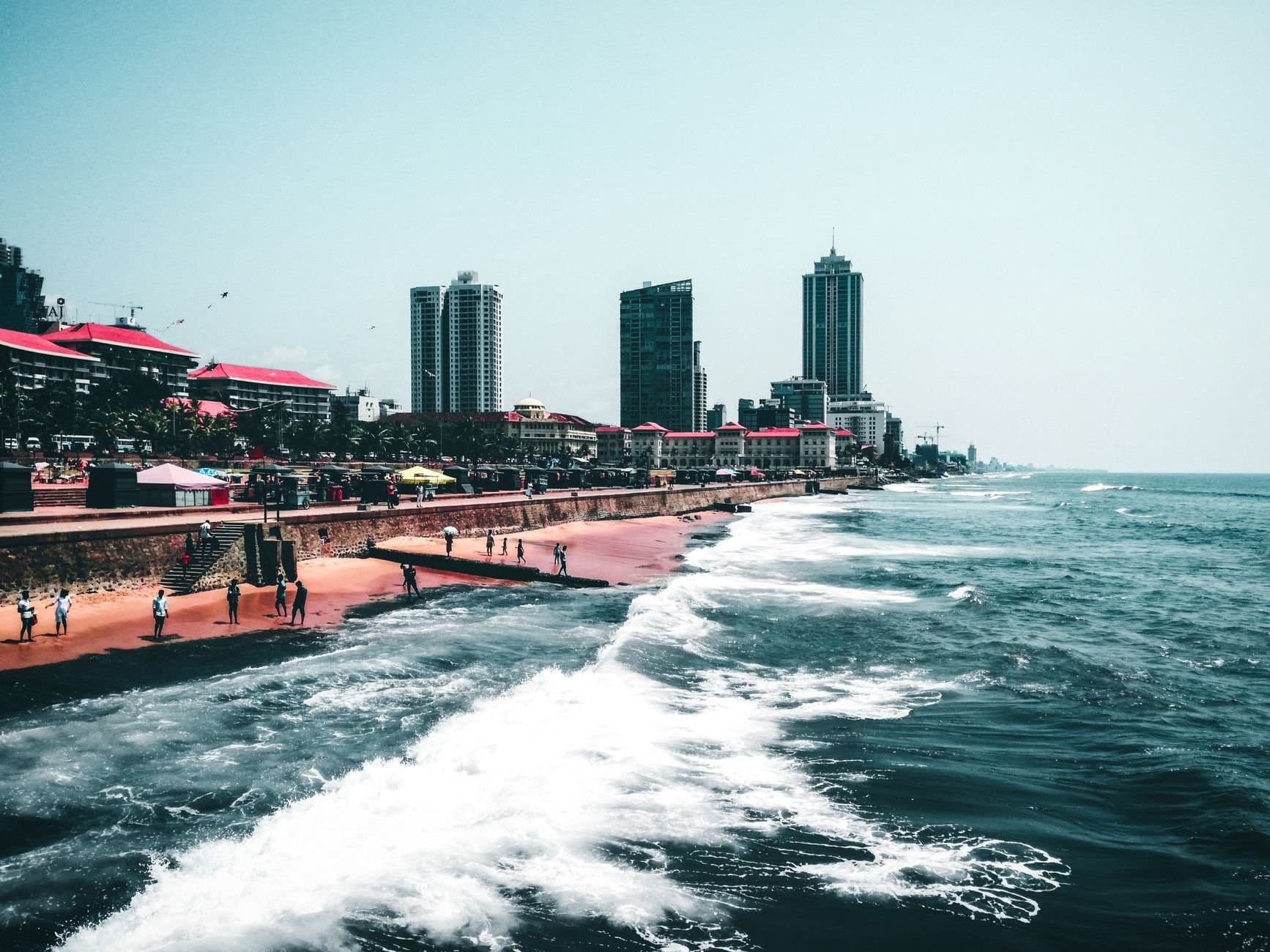 Scenic view of a coastal city with tall buildings and waves crashing against the shore.