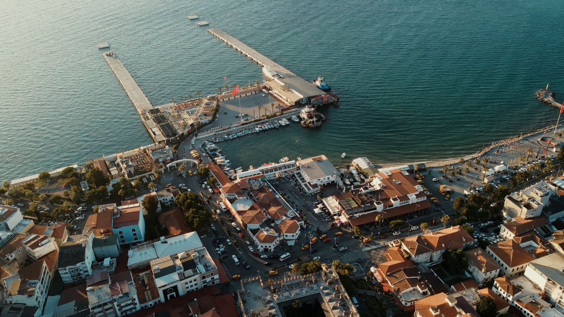 Stunning aerial view of Kuşadası harbor, Türkiye during the golden hour with vibrant waterfront and cityscape.