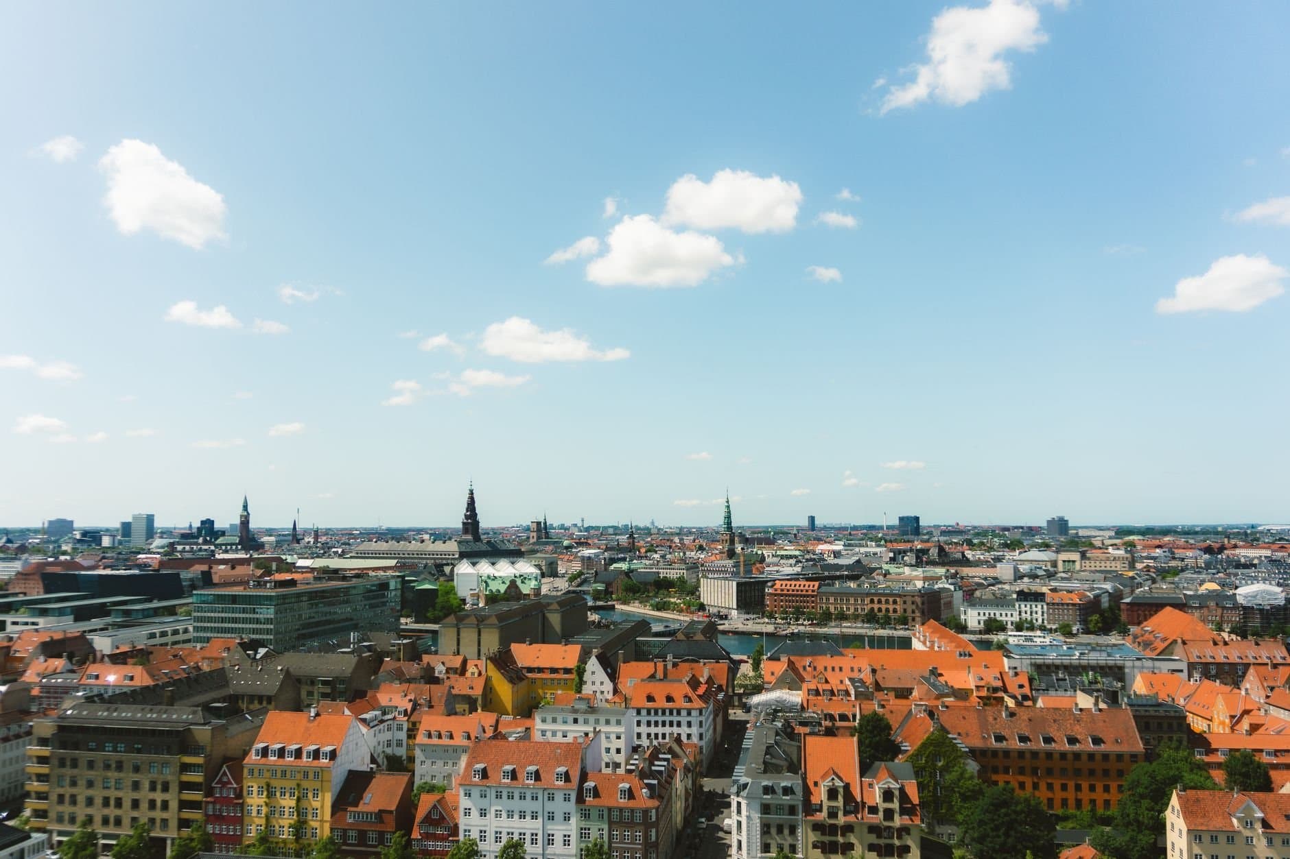 A picturesque aerial view of Copenhagen's colorful rooftops and skyline under a bright blue sky.