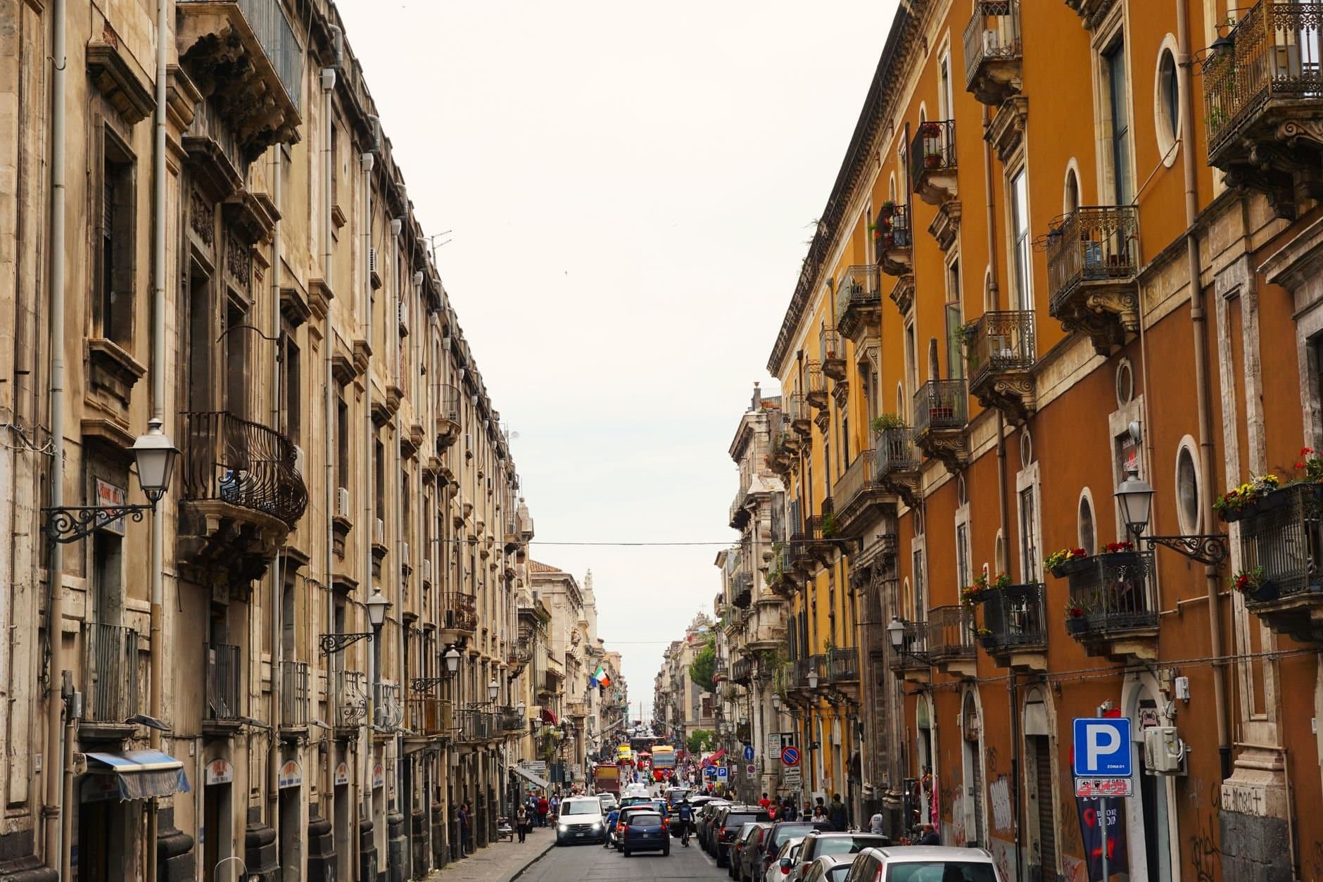 Charming city street with historic buildings and ornate balconies, bustling with vehicles and pedestrians.