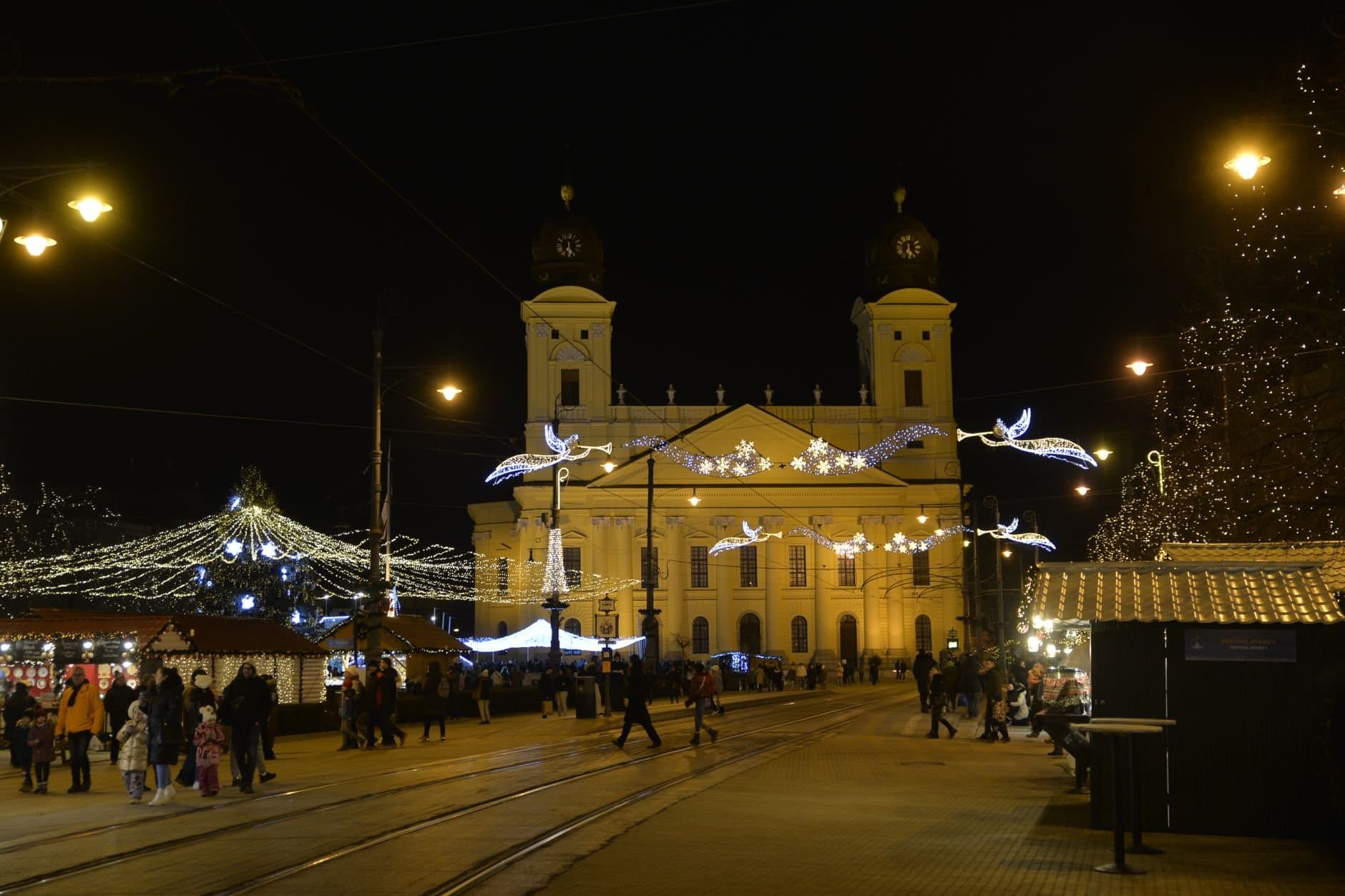 Night view of Debrecen Reformed Church adorned with festive Christmas lights and bustling holiday market.
