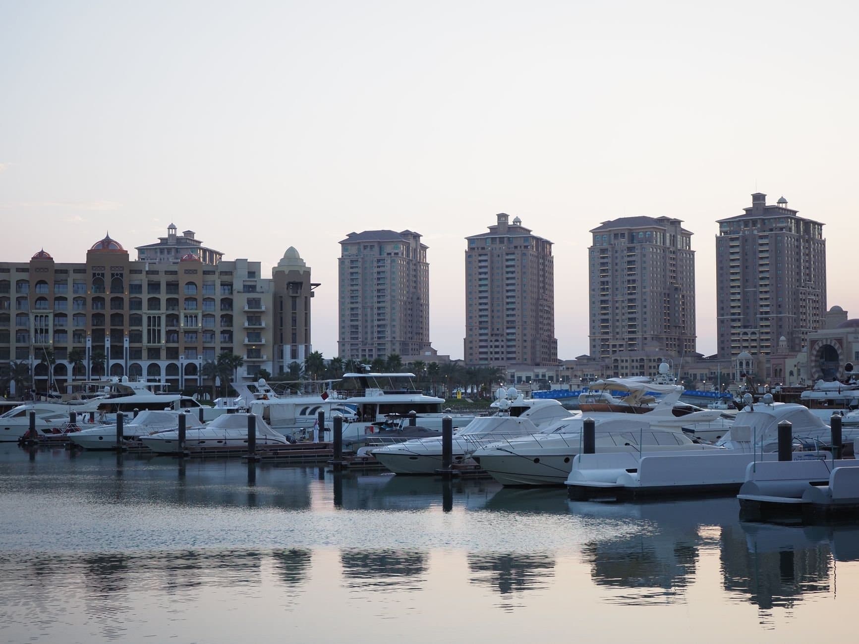 Beautiful evening view of luxury yachts at a marina in Doha, Qatar with tall buildings in the background.