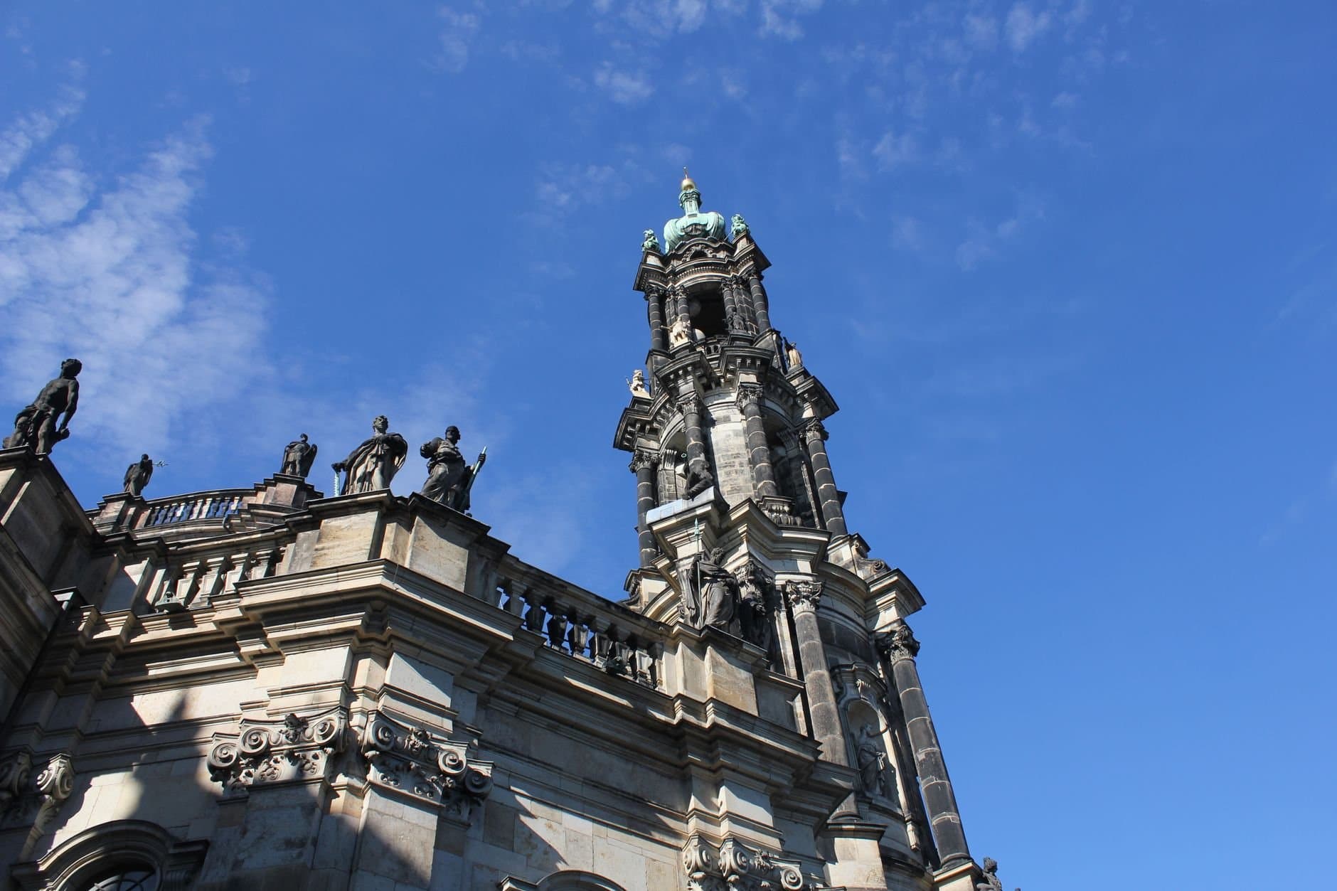 View of the Dresden Cathedral tower with ornate sculptures under a clear blue sky.