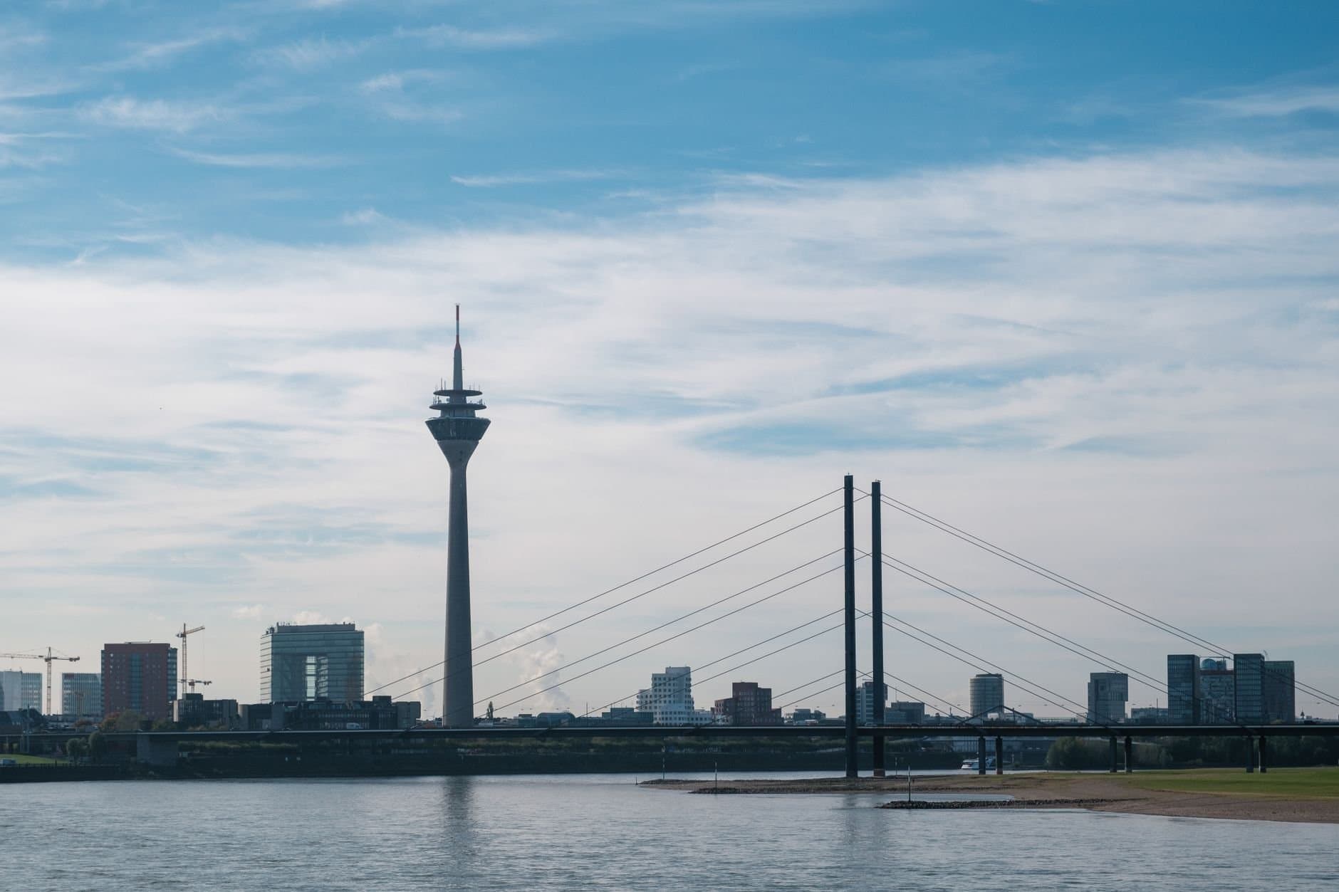Skyline view of Düsseldorf with Rheinturm and bridge spanning the Rhine under a clear blue sky.
