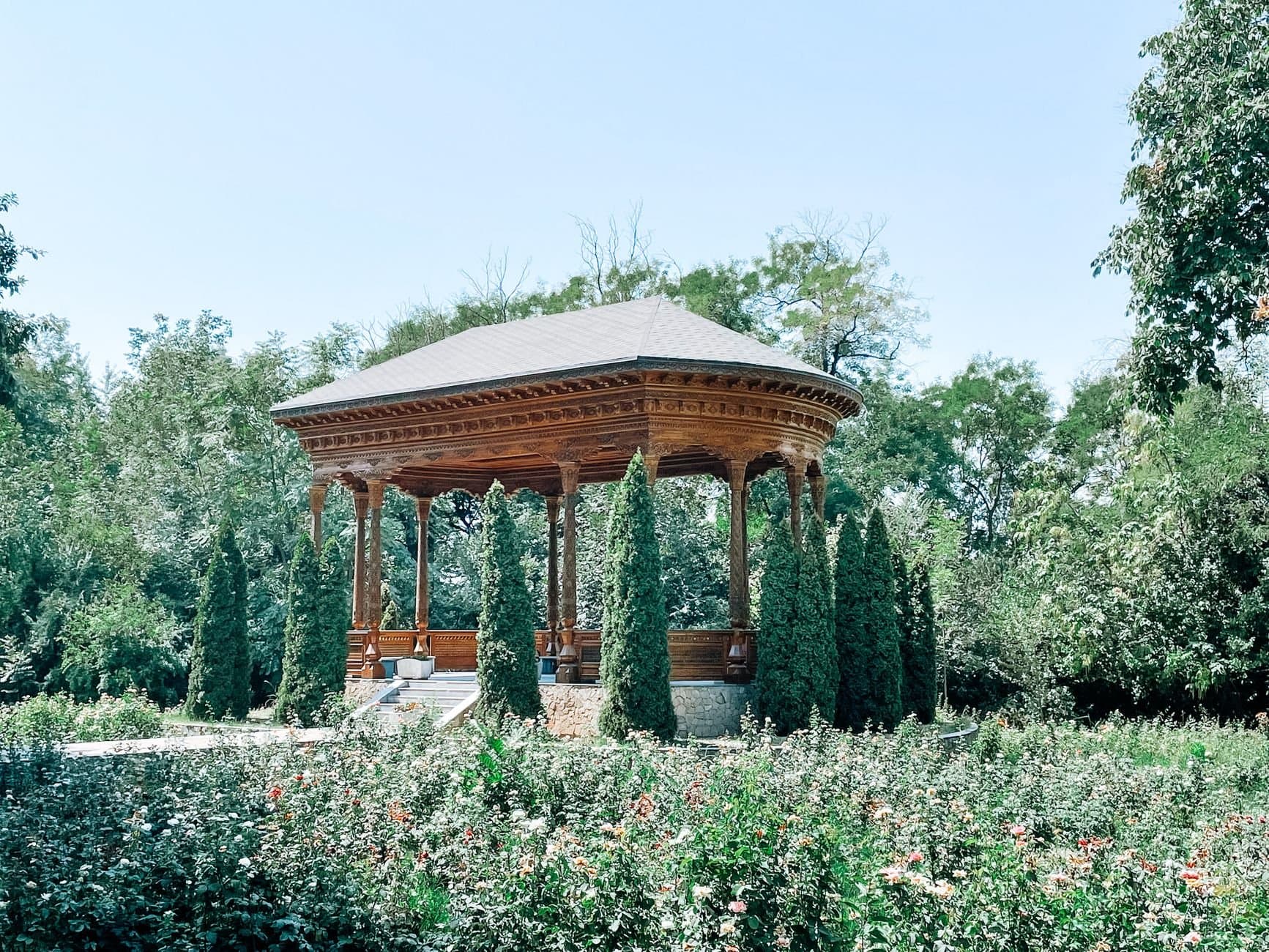 A wooden pavilion surrounded by greenery in a summer garden in Dushanbe, Tajikistan.
