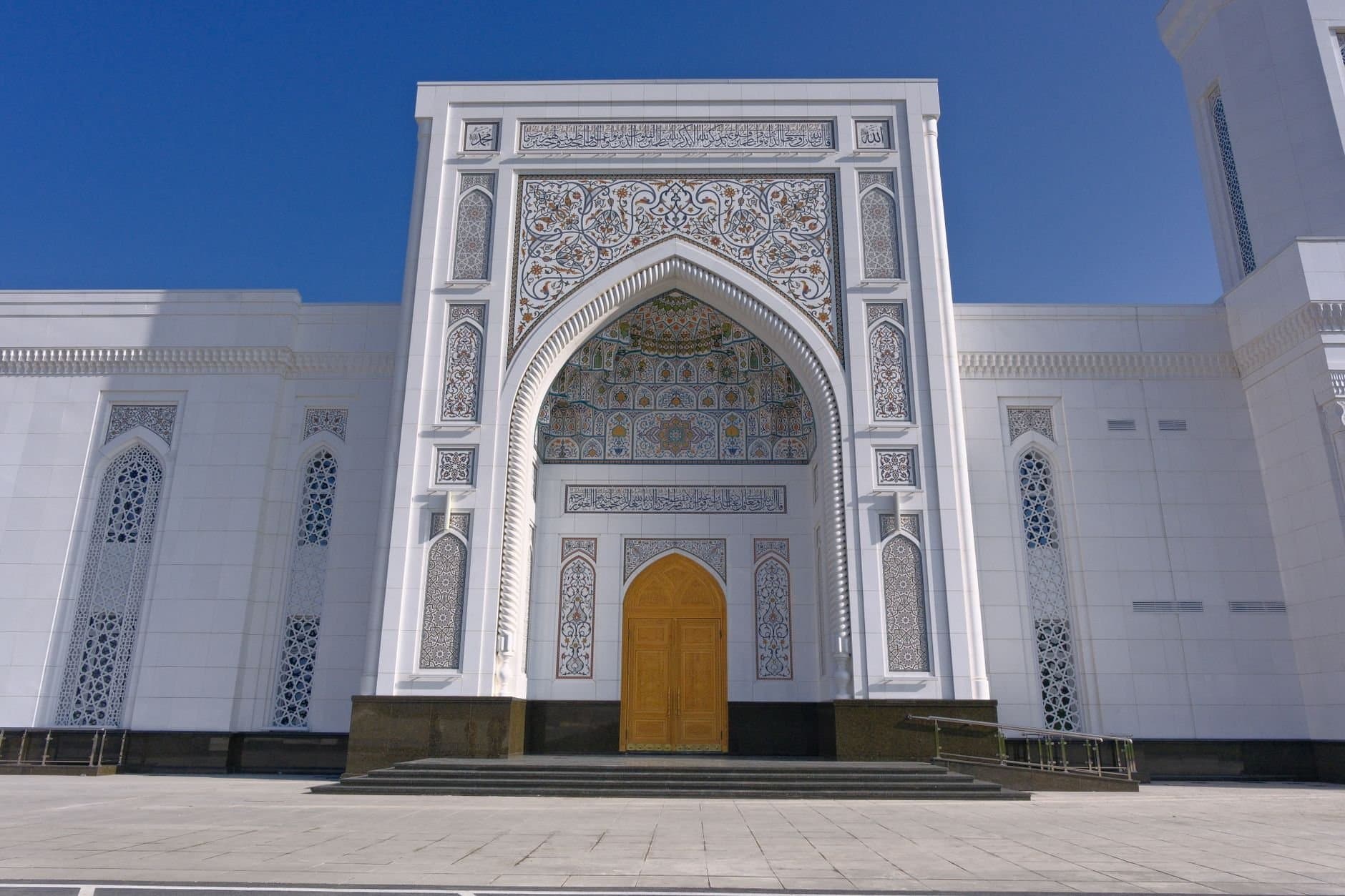 Stunning mosque facade with intricate designs under a clear blue sky, showcasing Islamic architecture.