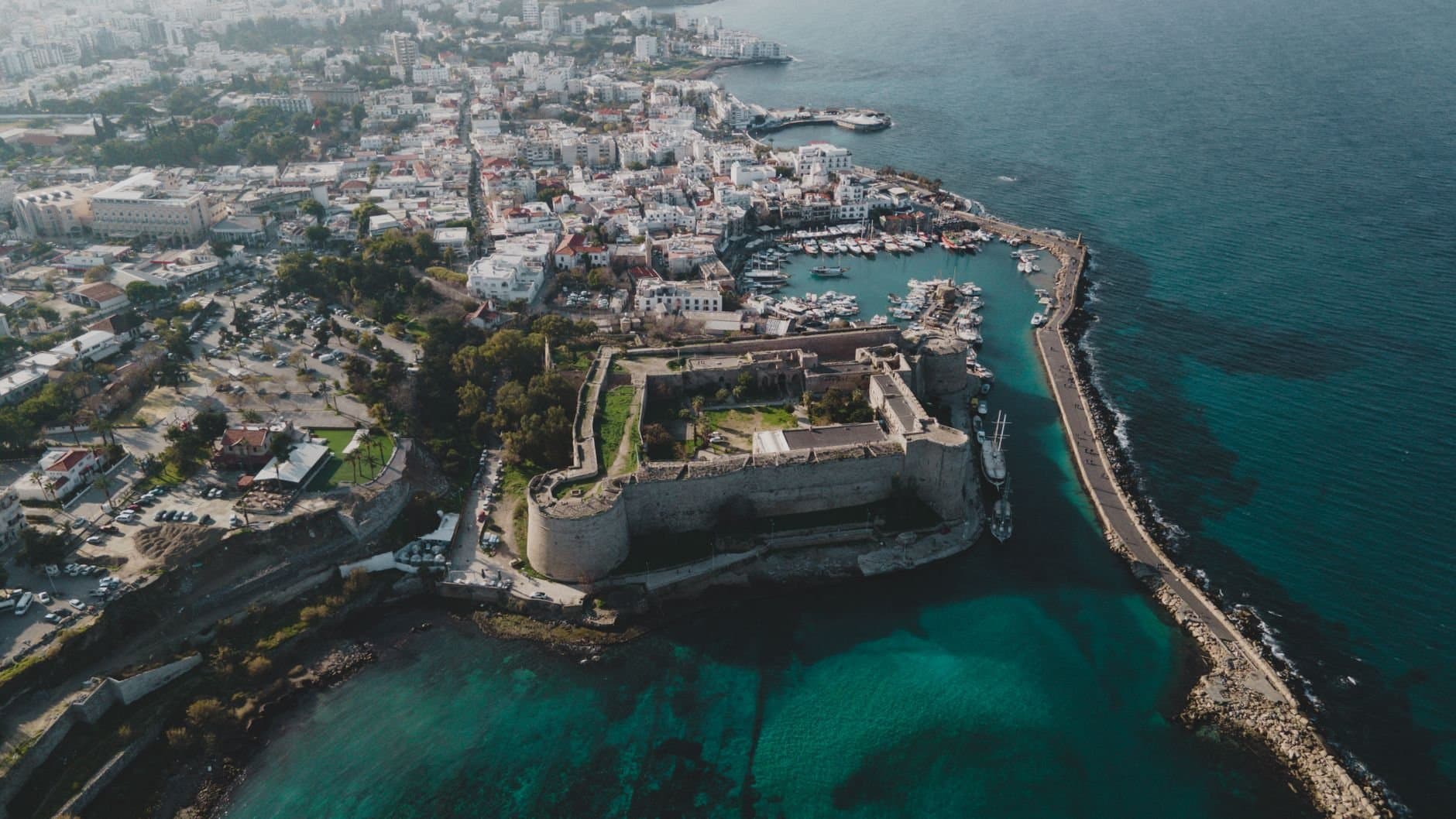Stunning aerial view of a historic coastal fortress surrounded by vibrant city life and deep blue sea.