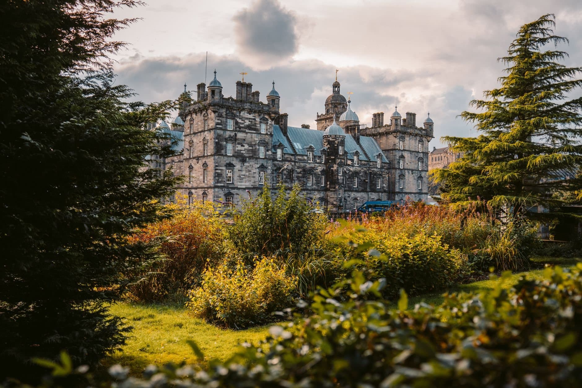 A picturesque view of an ancient castle surrounded by vibrant greenery under a cloudy sky.