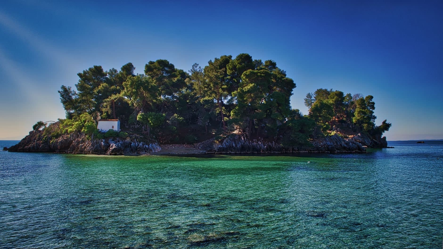 Discover the serene beauty of an untouched Greek island surrounded by clear azure waters and lush green foliage.