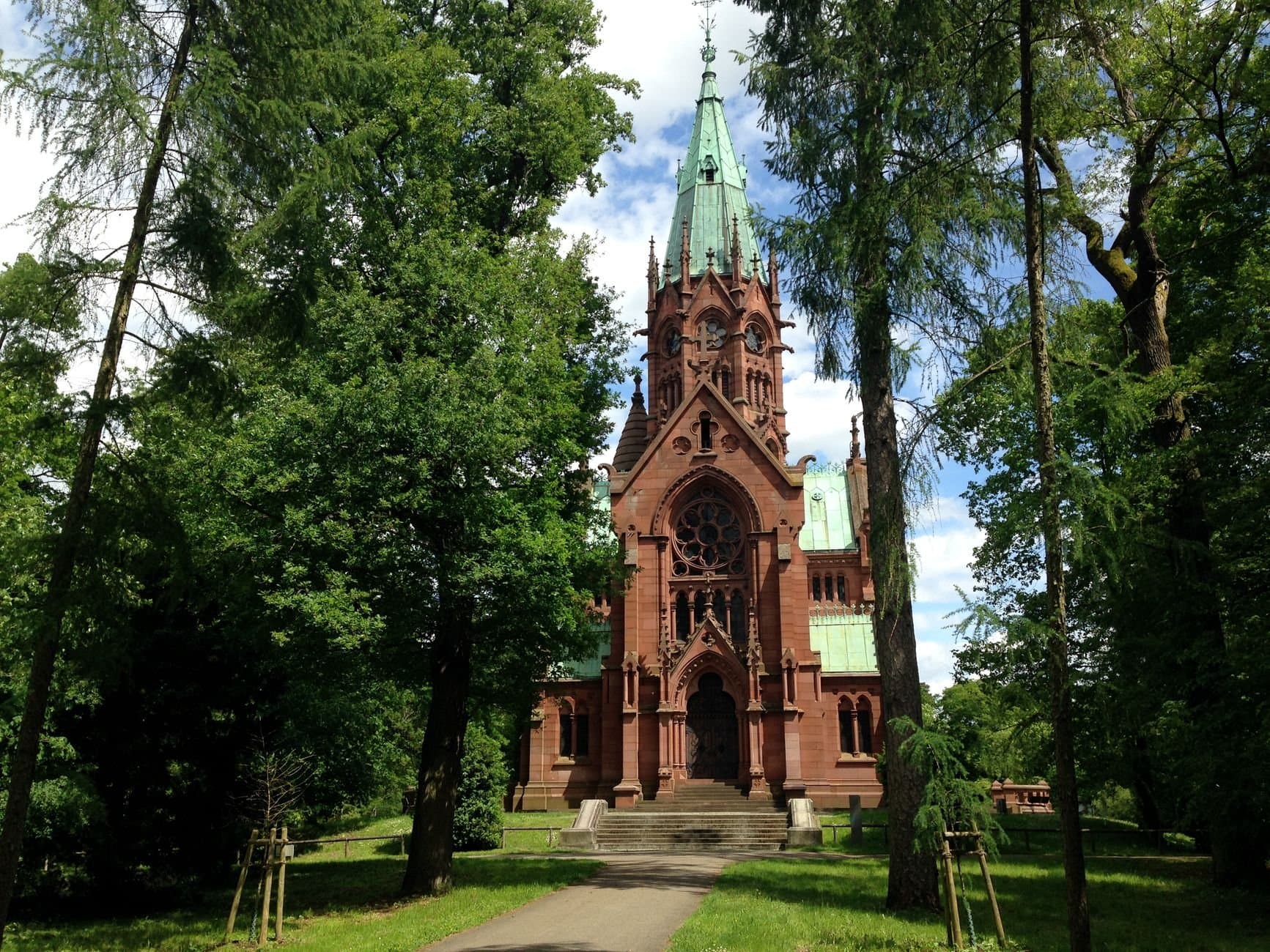 A stunning red brick chapel amidst lush greenery under a vibrant blue sky.