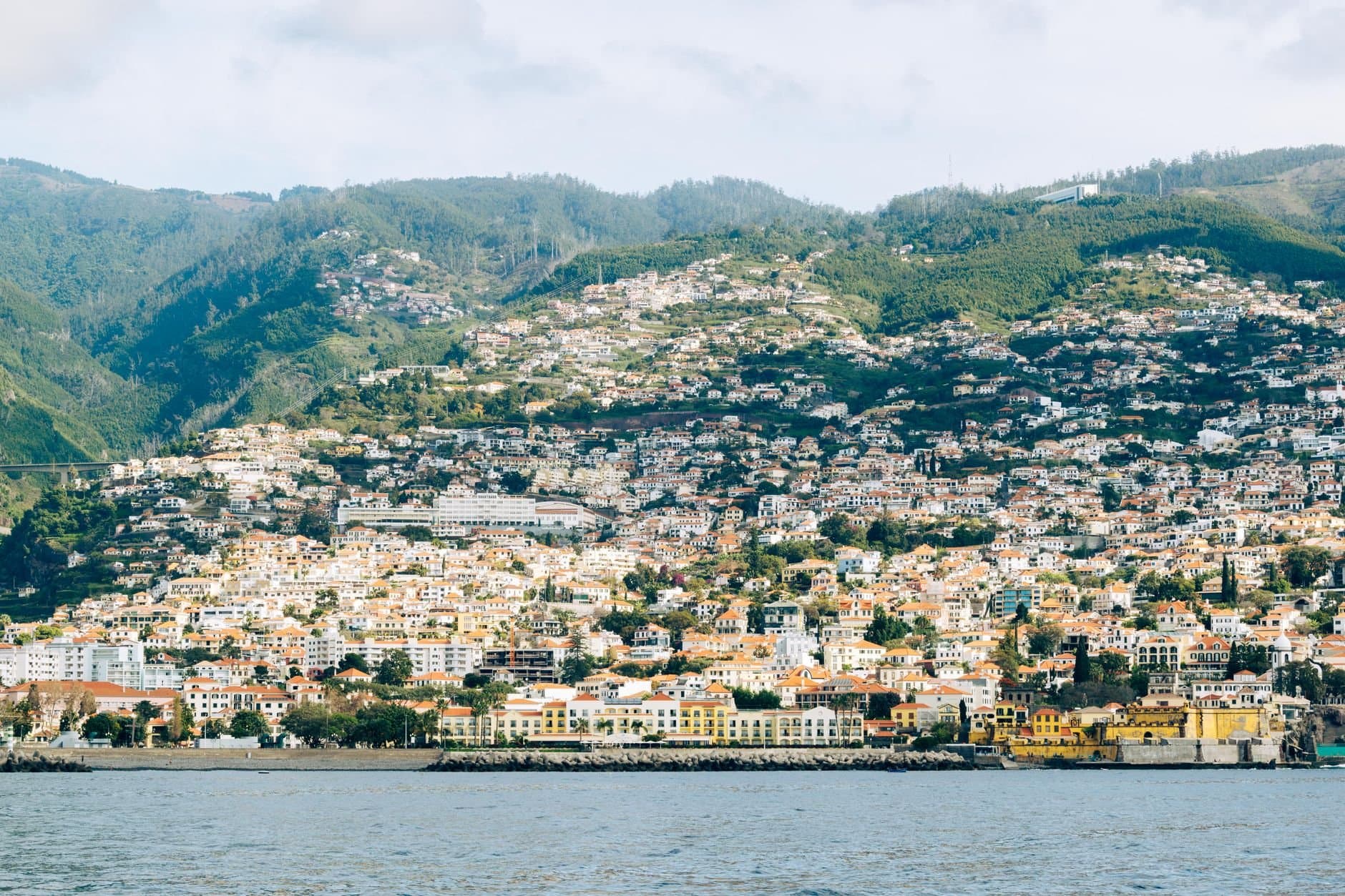 Scenic view of Madeira's hillside urban landscape with vibrant architecture and lush green hills.