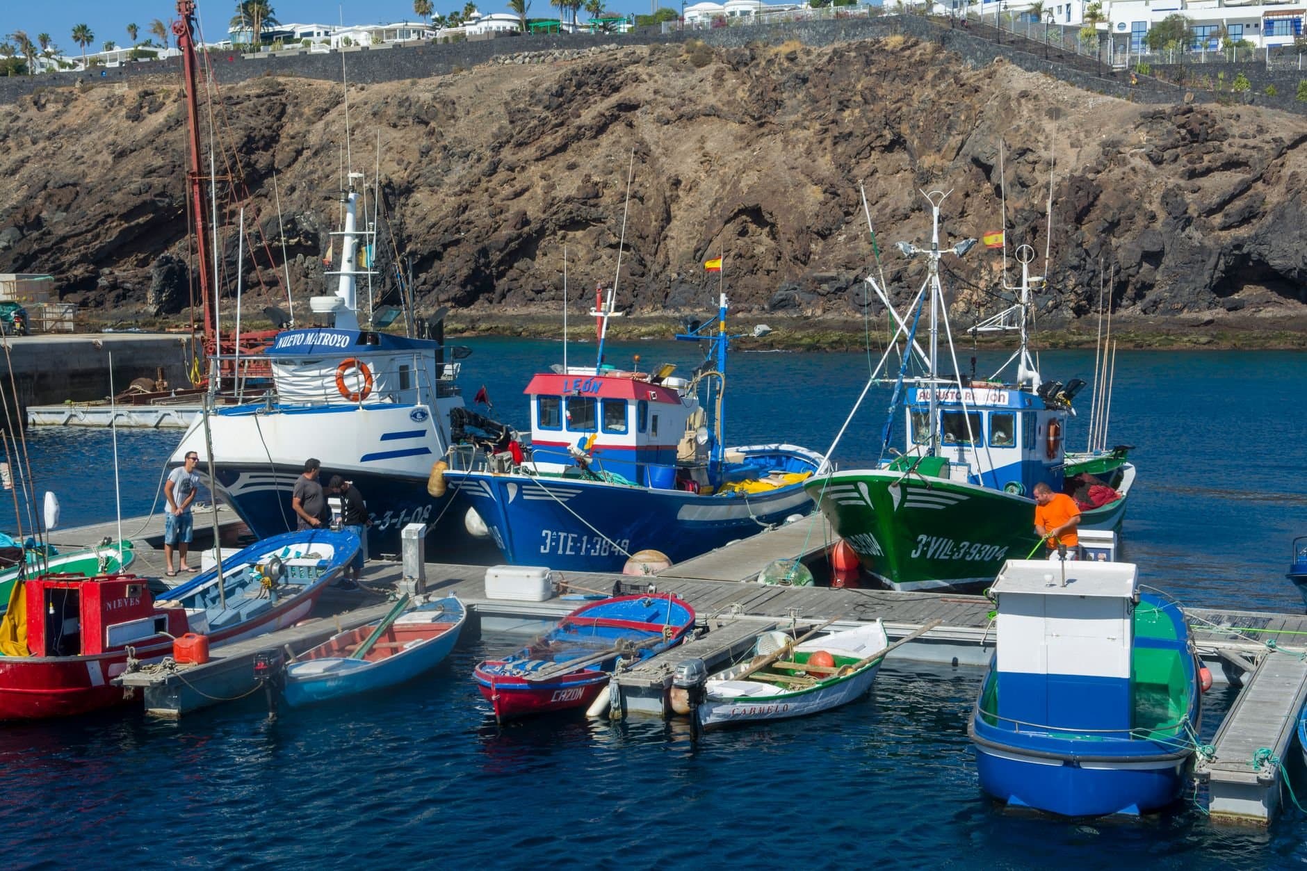Vibrant fishing boats docked at Puerto del Carmen marina with rocky cliff backdrop, showcasing coastal life.