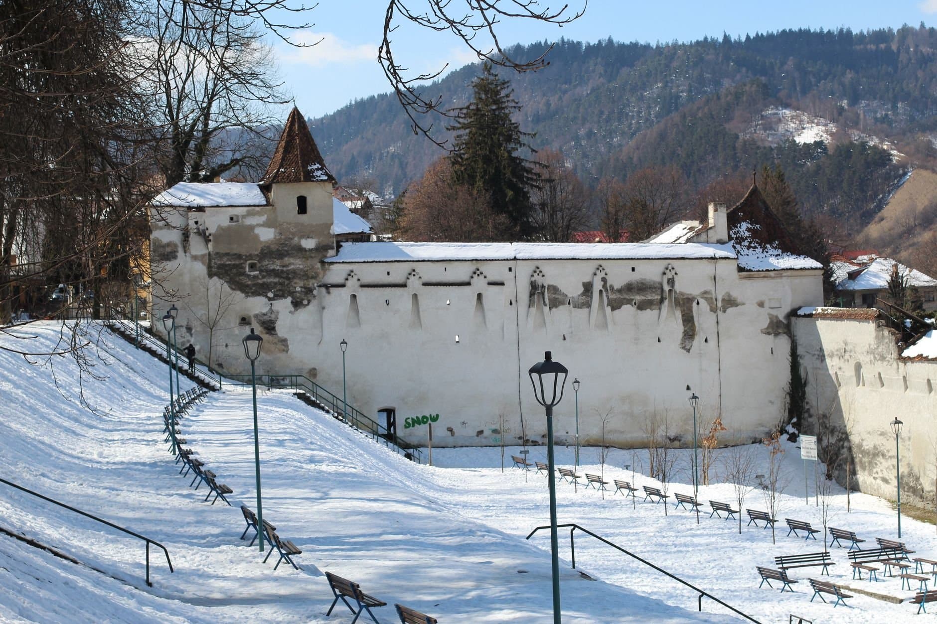 A snowy winter scene at Weaver Bastion in Brasov with benches and fortress walls.