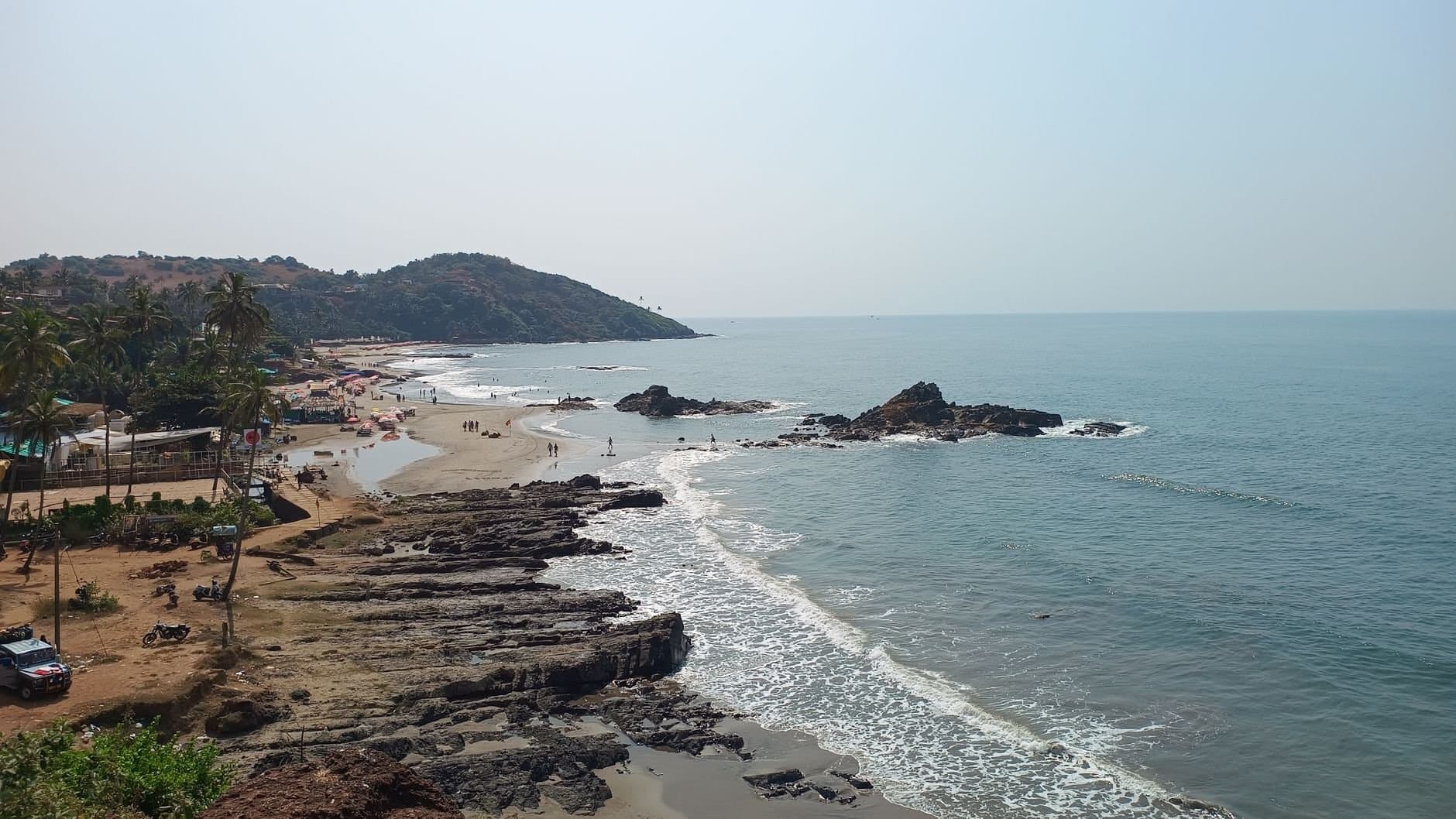 Explore the serene Anjuna Beach in Goa, showcasing beautiful sandy shores and rocky coastline.
