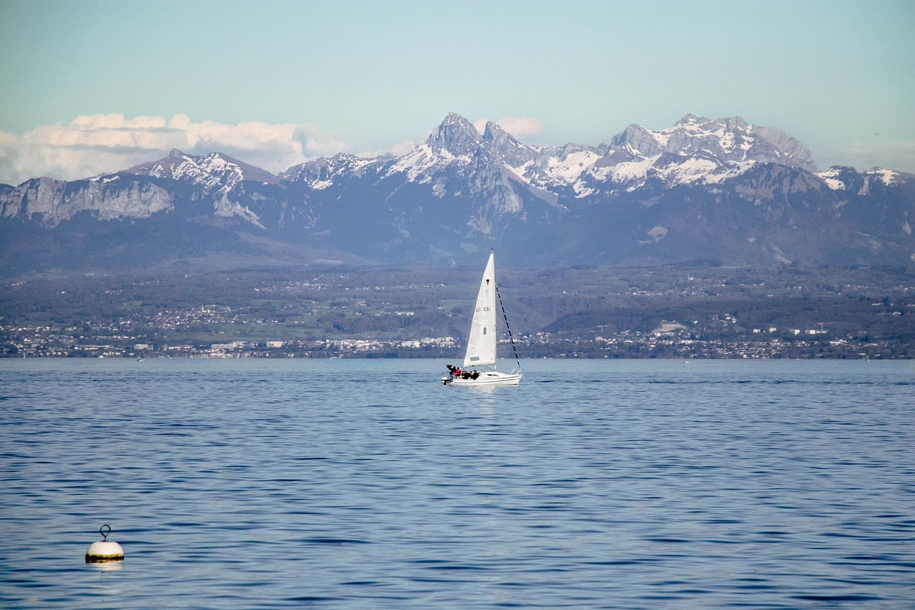 A sailboat glides on Lake Geneva with the majestic Alps in the background, capturing serene nature.