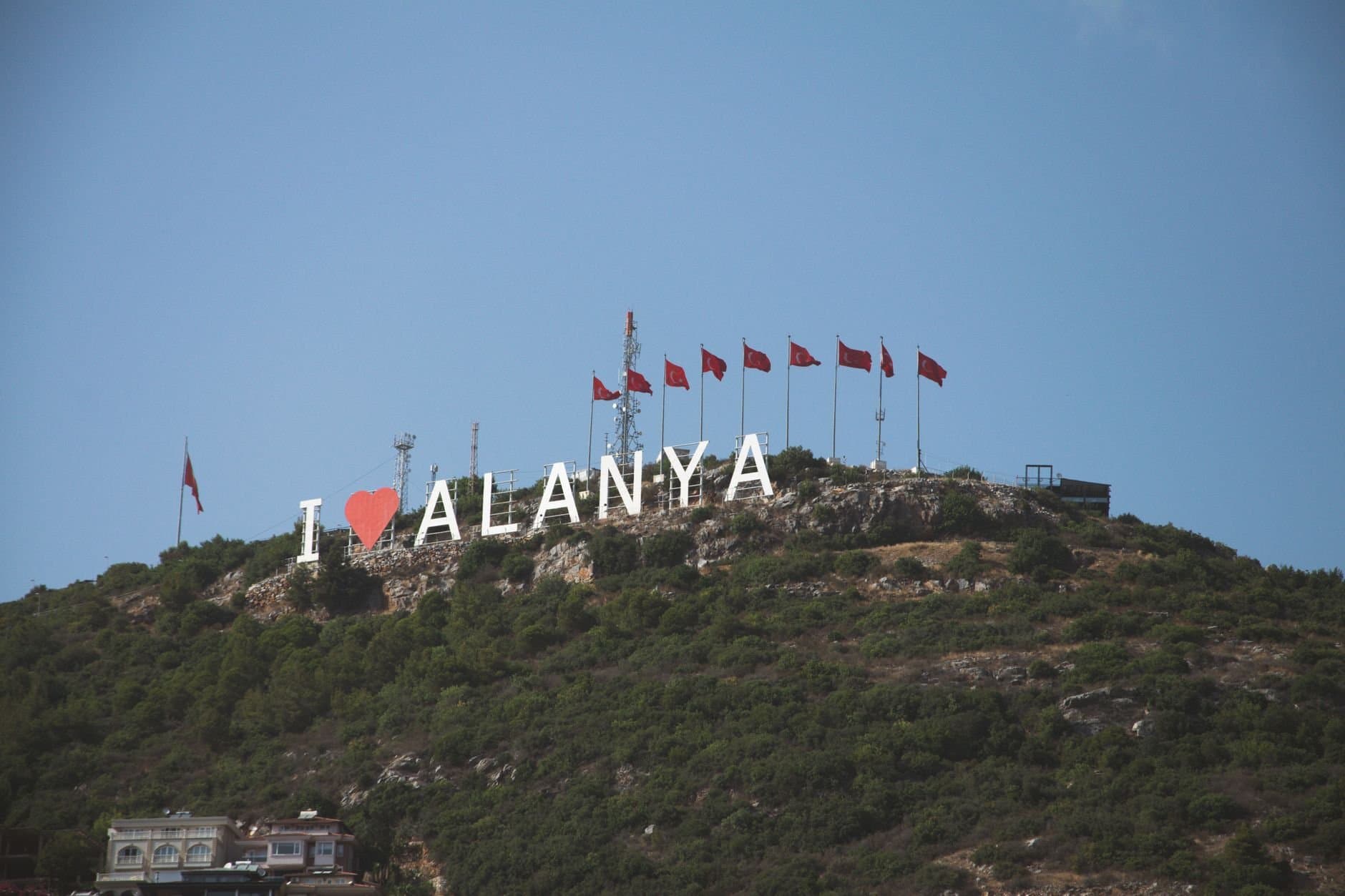 A picturesque view of the famous 'I Love Alanya' sign on a hill with Turkish flags in Türkiye.