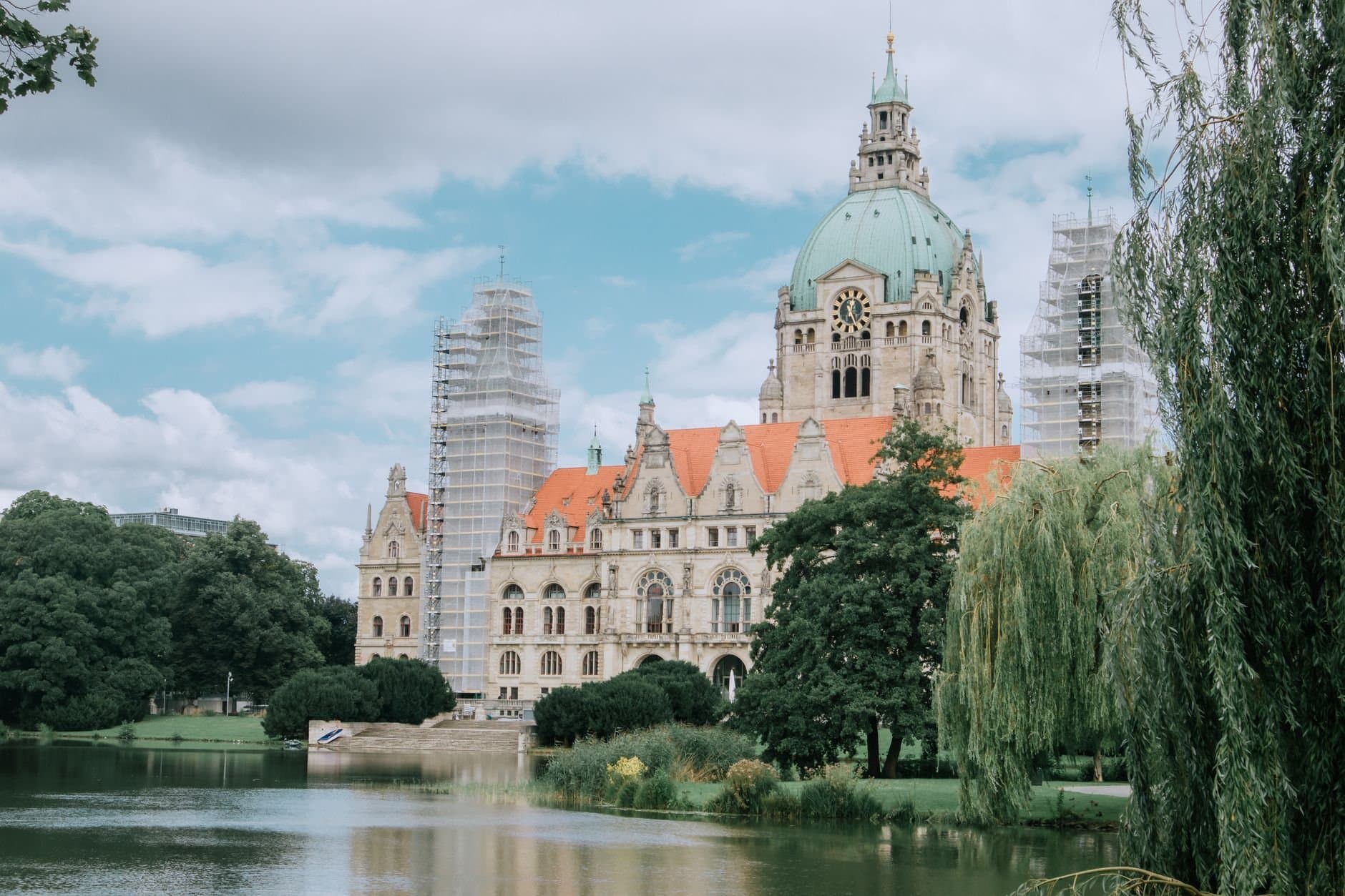 Historic building with dome and red roof by a tranquil lake, showcasing beautiful architecture.