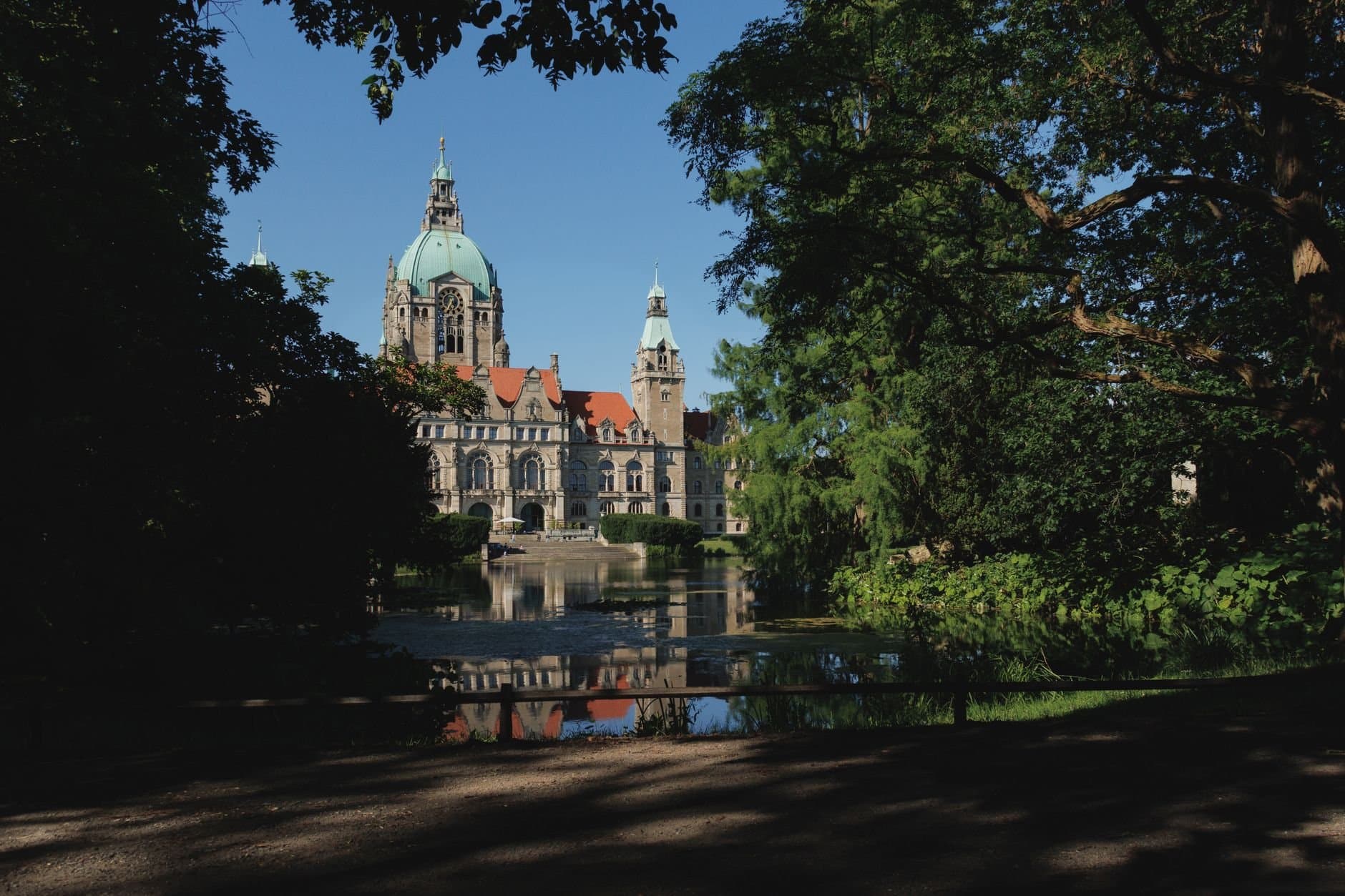 The New Town Hall in Hannover framed by lush trees and reflected in a serene lake.