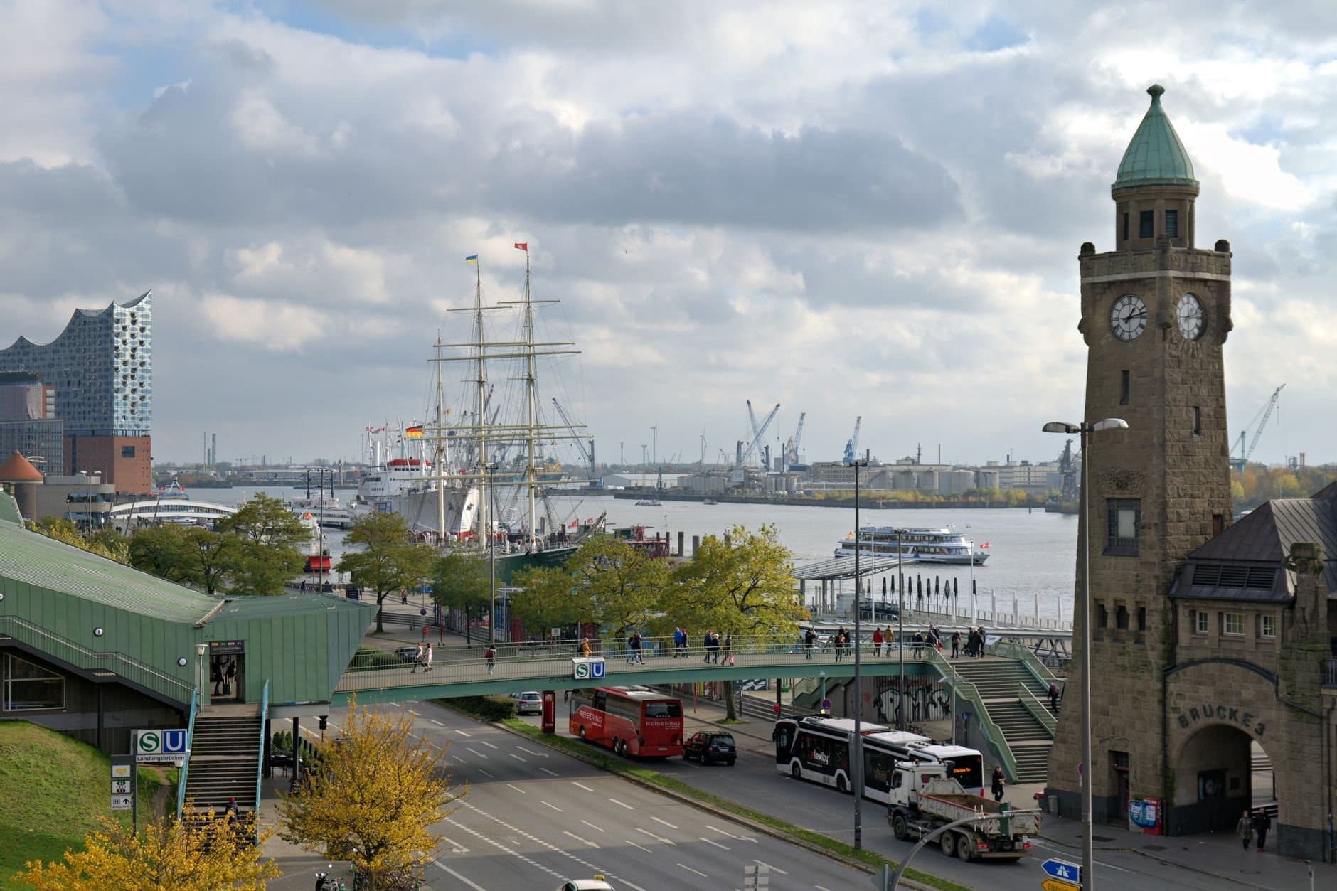 A busy day at Hamburg's harbor featuring the Elbphilharmonie, historic ships, and clock tower.