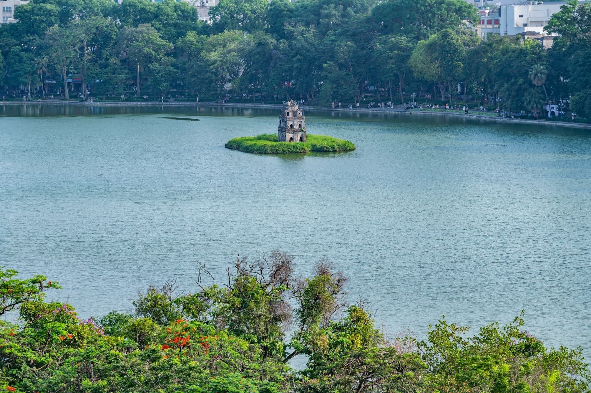 A scenic view of Turtle Tower on Hoan Kiem Lake surrounded by lush greenery in Hanoi, Vietnam.