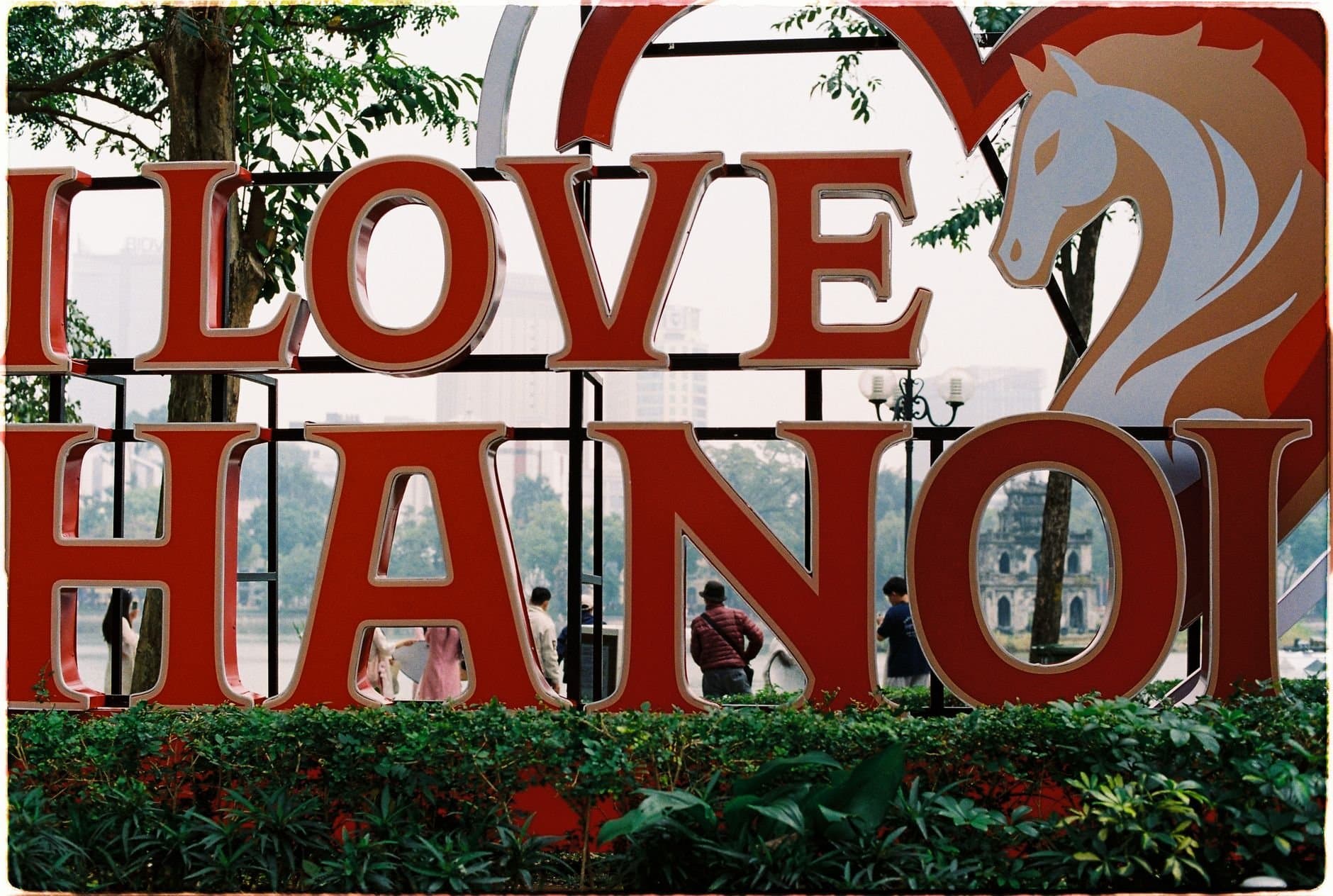 Colorful 'I Love Hanoi' sign with people in urban park setting, showcasing Hanoi's charm.