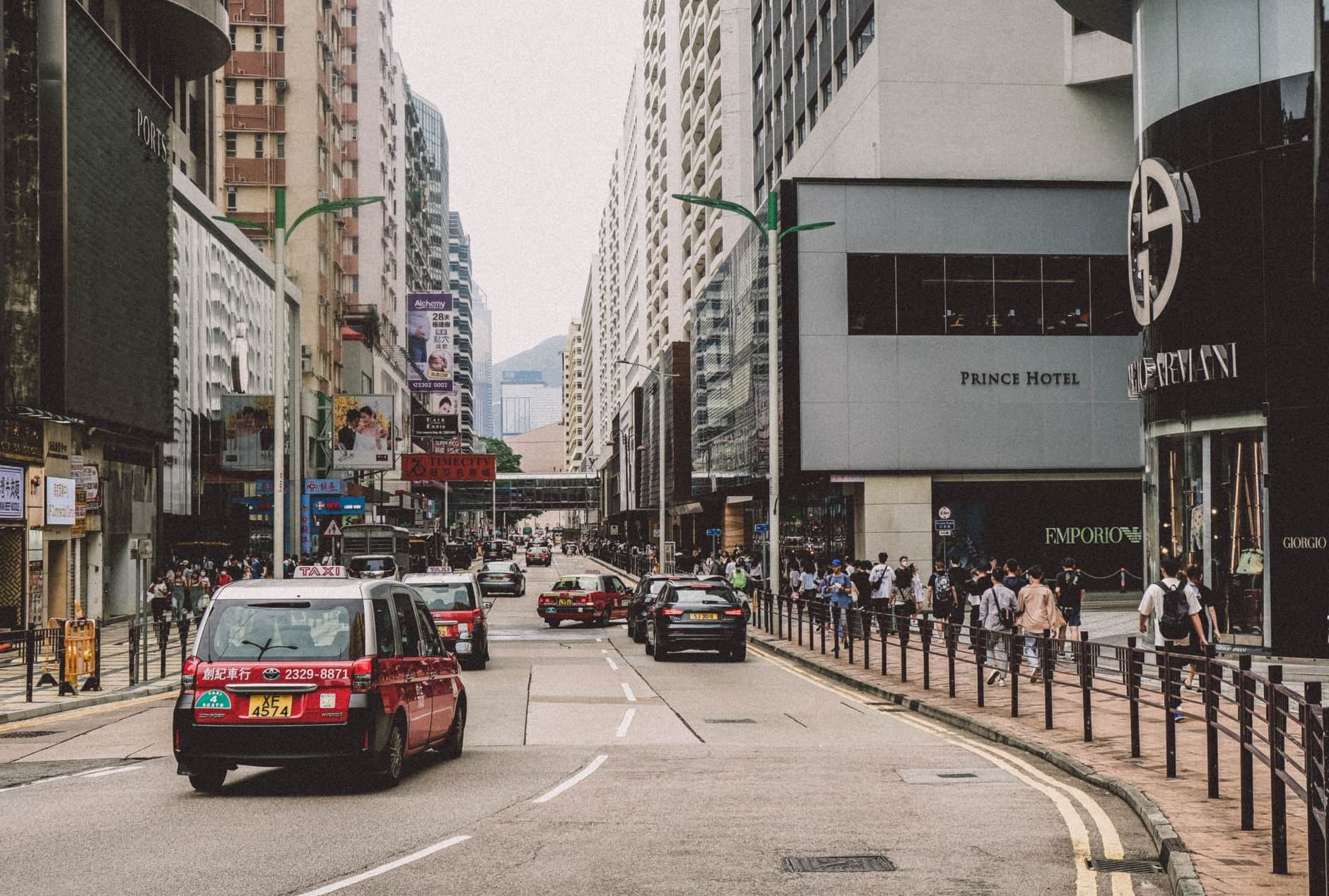 A vibrant city street scene with bustling traffic and busy sidewalks, featuring urban architecture.