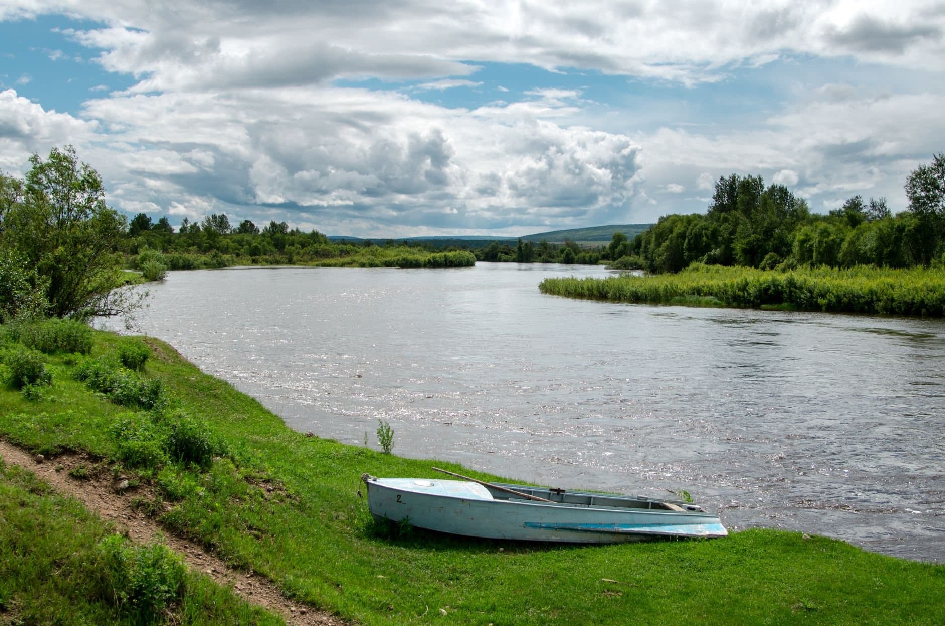 Peaceful riverside landscape featuring a boat on a grassy bank under a cloudy sky in rural Russia.