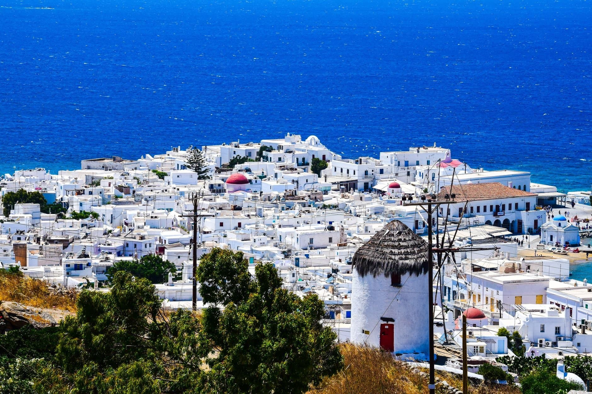 A stunning bird's-eye view of white buildings in Mykonos Town overlooking the blue Aegean Sea.
