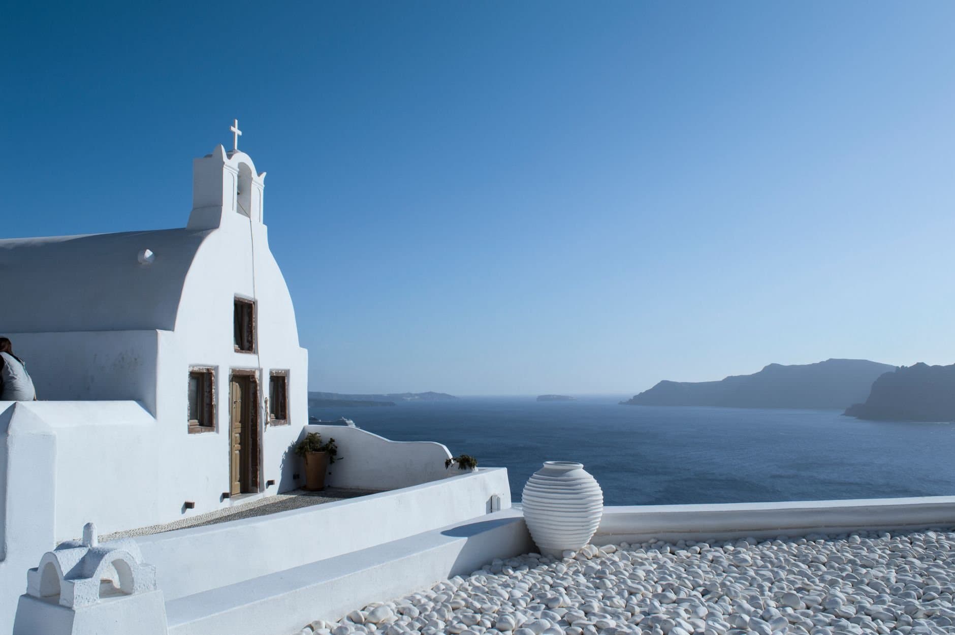 Whitewashed church in Santorini with panoramic Aegean Sea view under a clear blue sky.