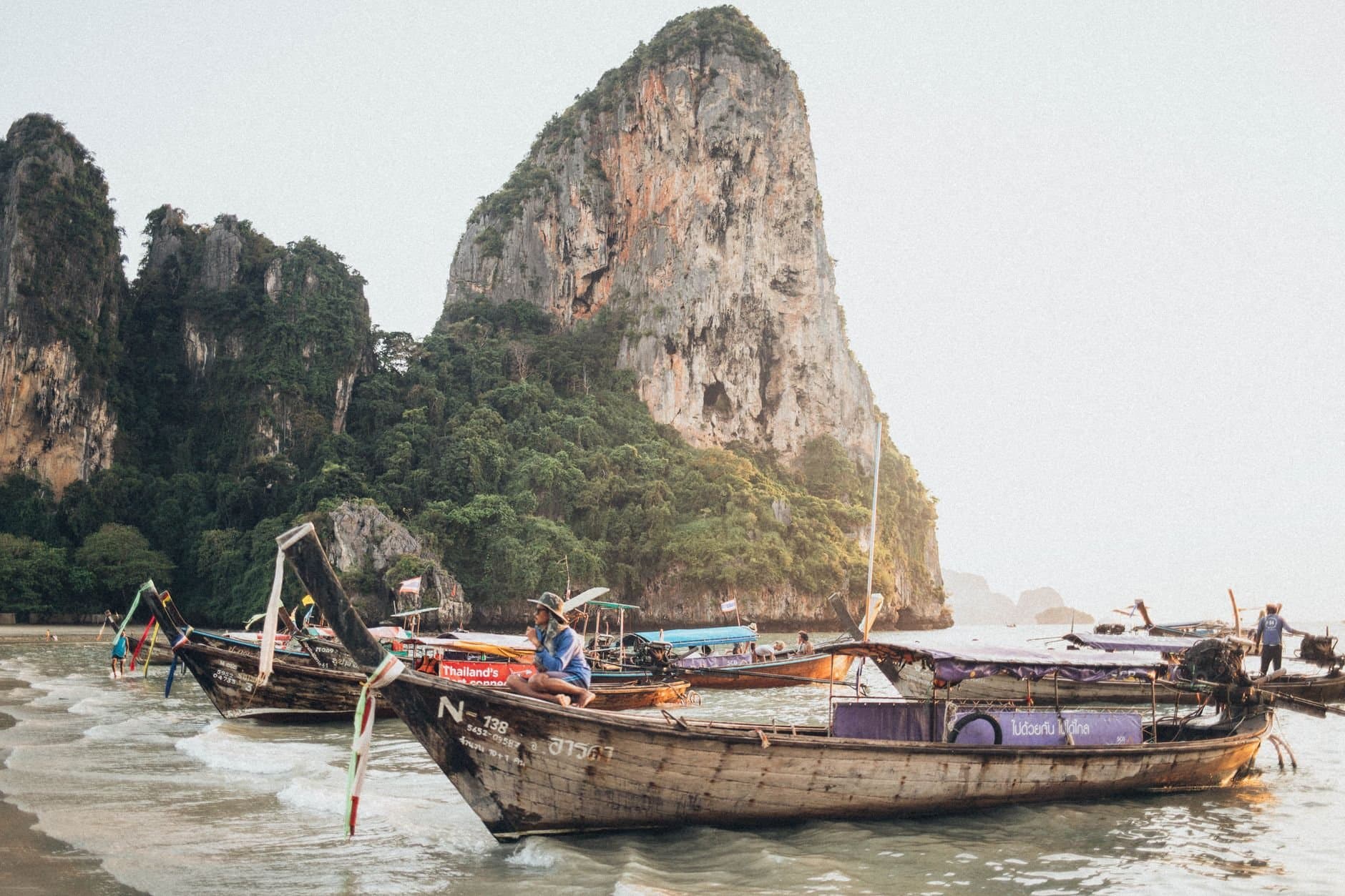 Explore the stunning scenery and traditional long-tail boats in Krabi, Thailand with majestic limestone cliffs in the background.