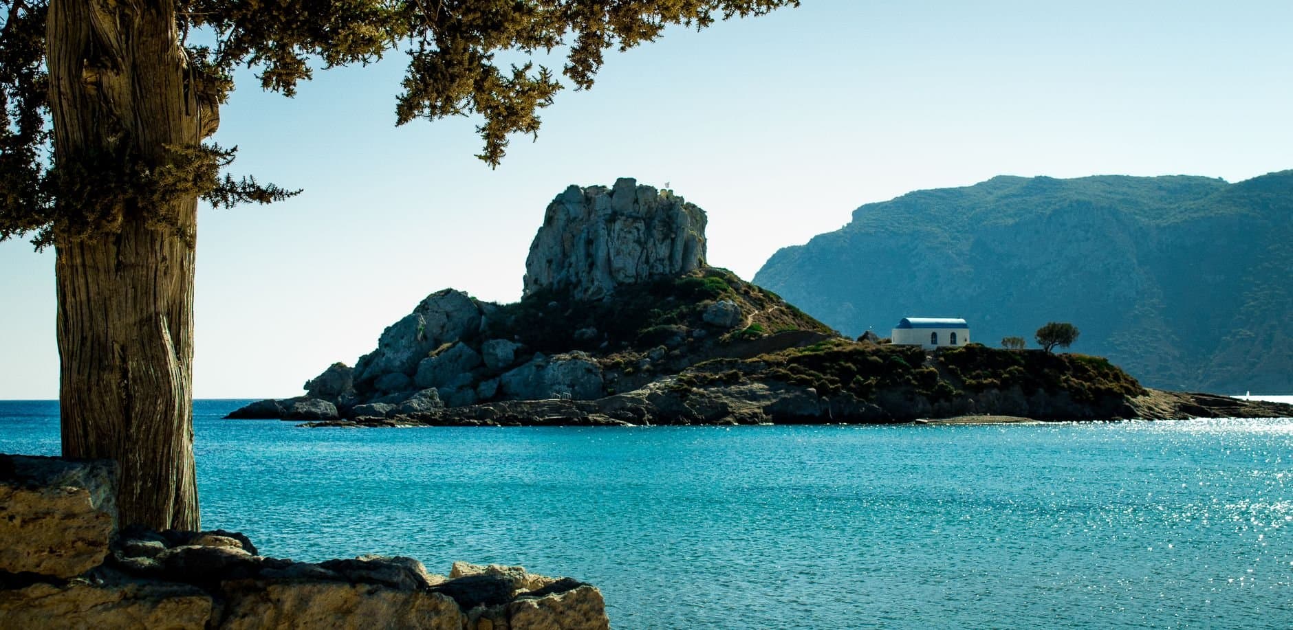 Beautiful coastal view of Kos, Greece featuring a rocky island and vibrant blue waters.