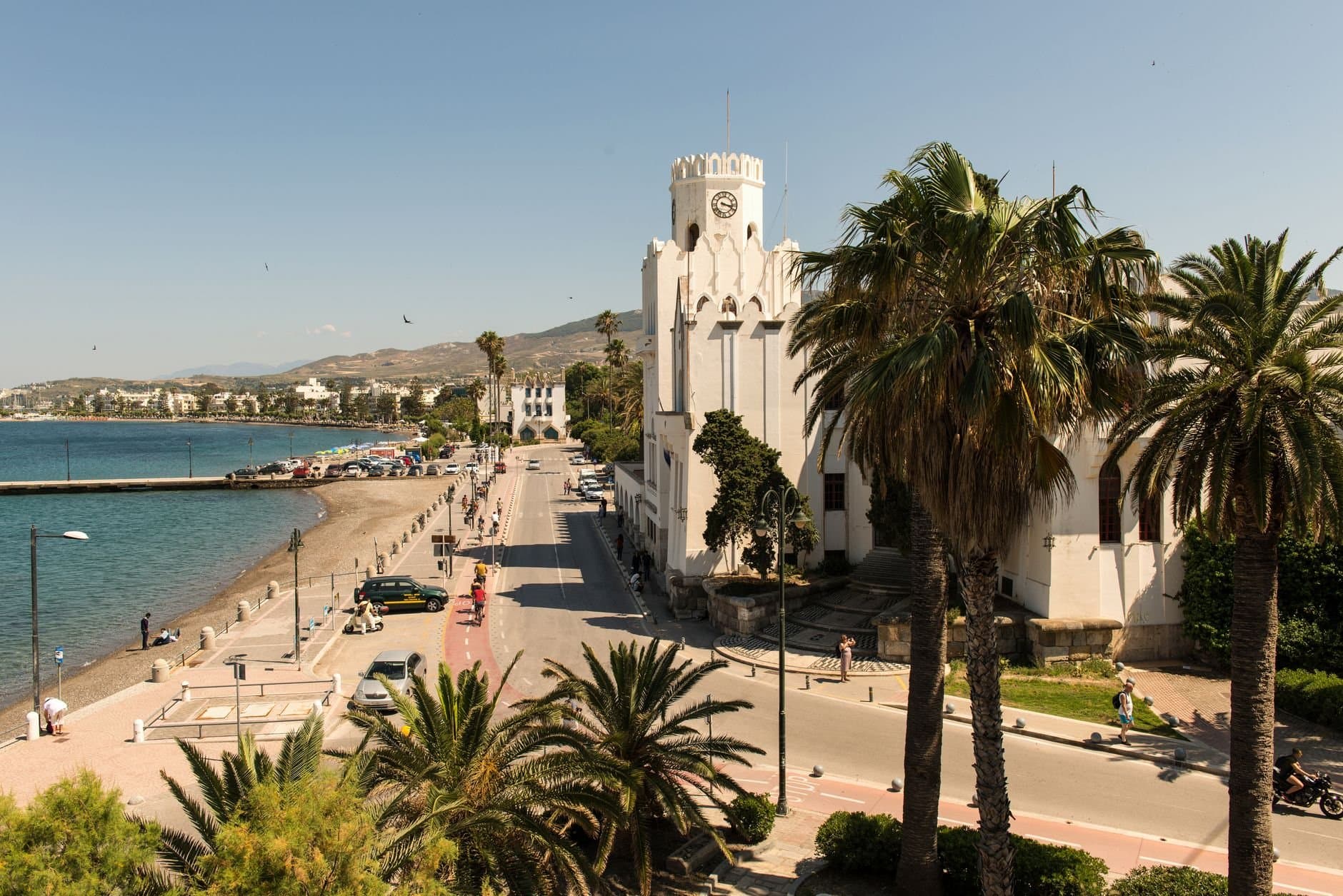 Charming street view of Kos, Greece with palm trees and historic architecture under a bright summer sky.