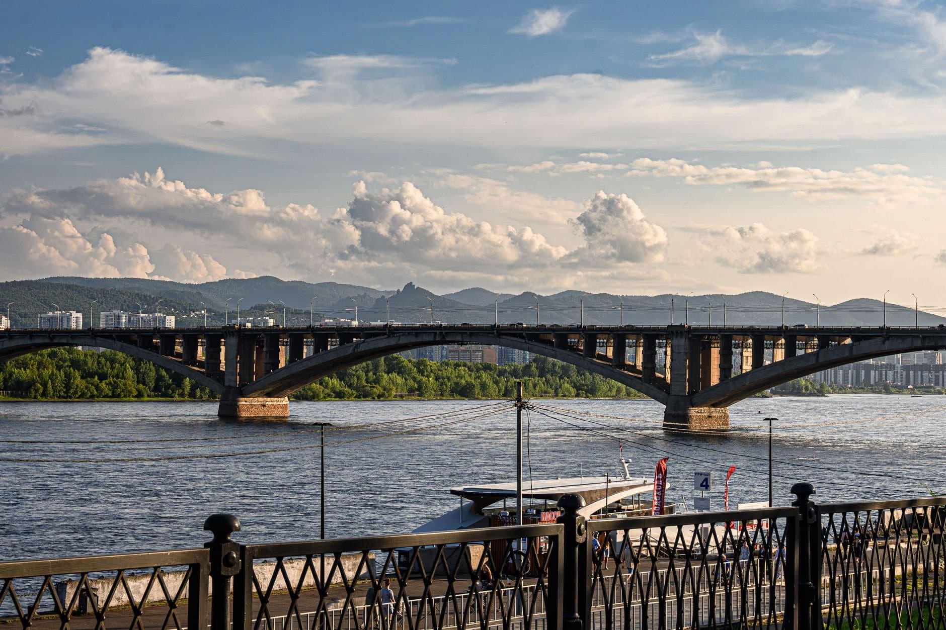 Beautiful view of a bridge spanning over a river with mountains in the background under a cloudy sky.