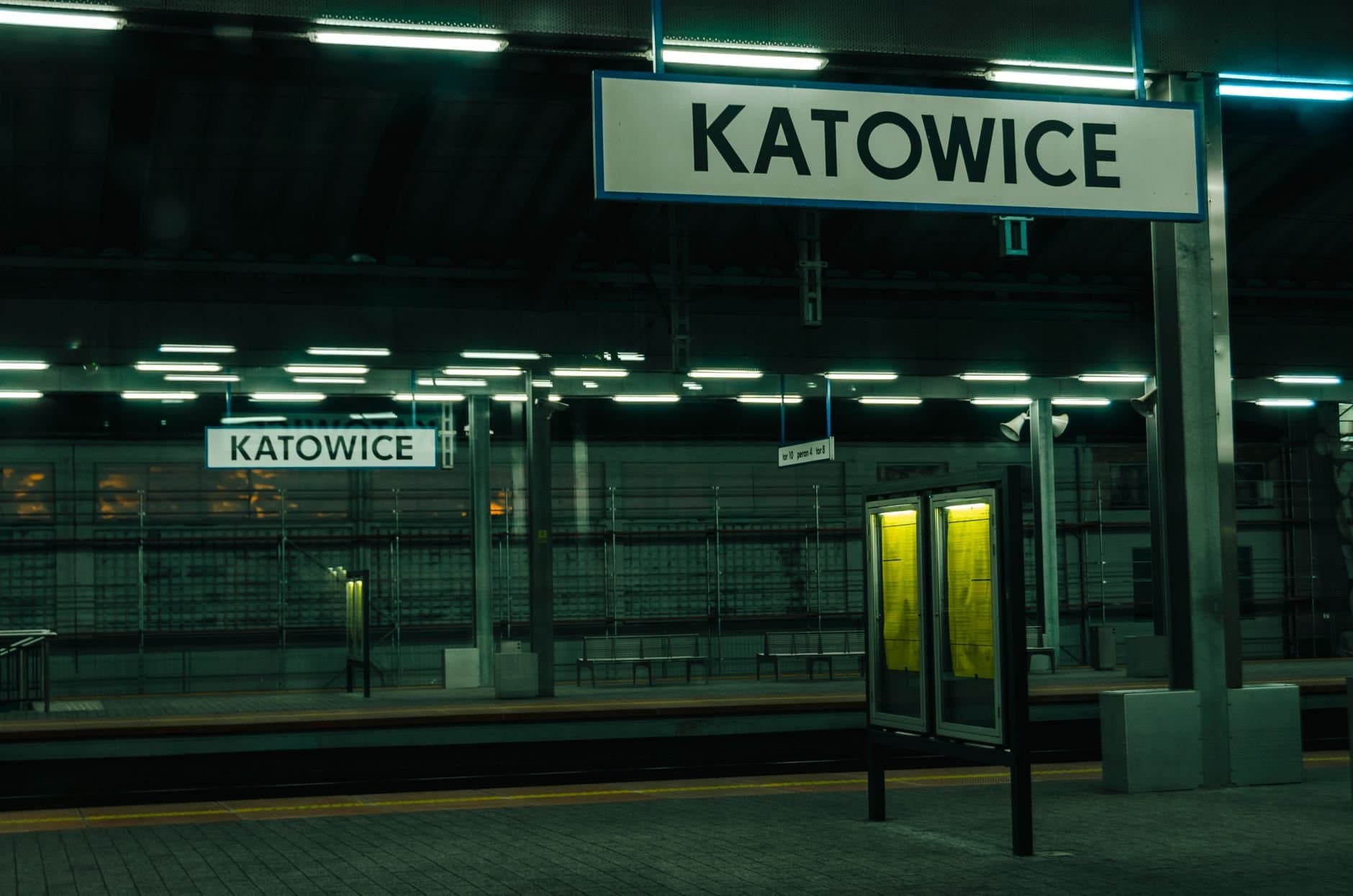 Moody night view of the platform at Katowice train station in Poland, highlighting signage.