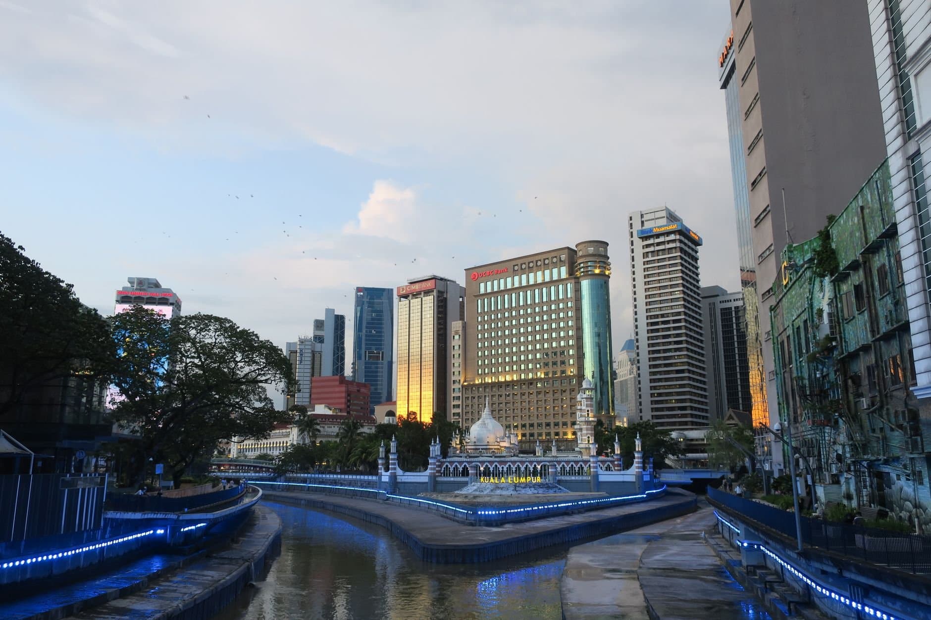 A stunning sunset view of Kuala Lumpur's skyline with a river in the foreground, showcasing modern architecture.