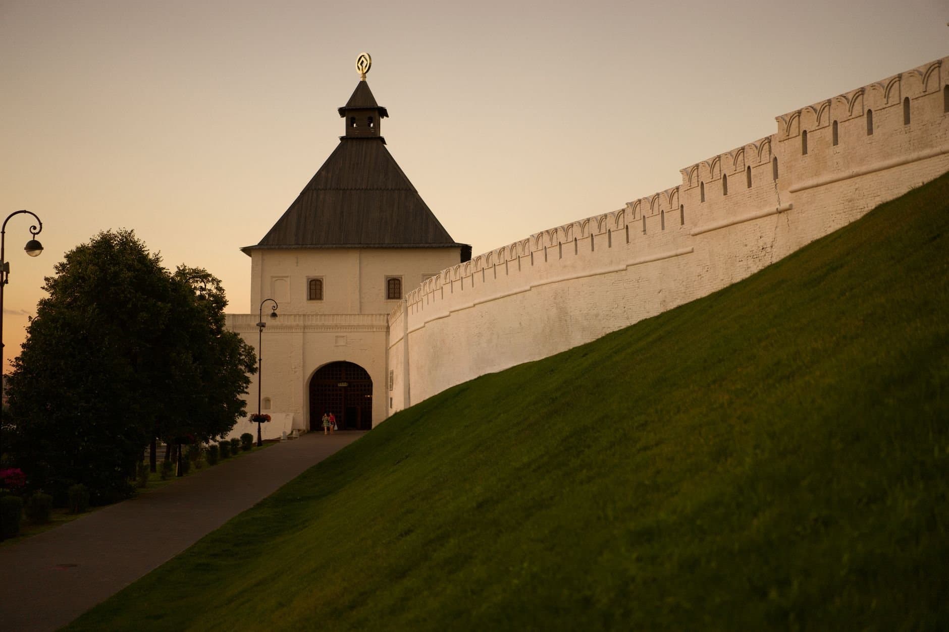 Capture of Kazan Kremlin's iconic wall and tower at sunset with lush greenery.