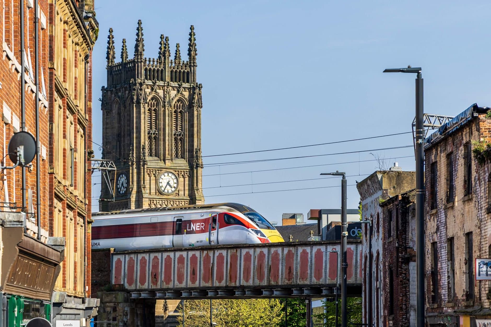 LNER train crossing near historic church tower in Leeds, England with urban background.