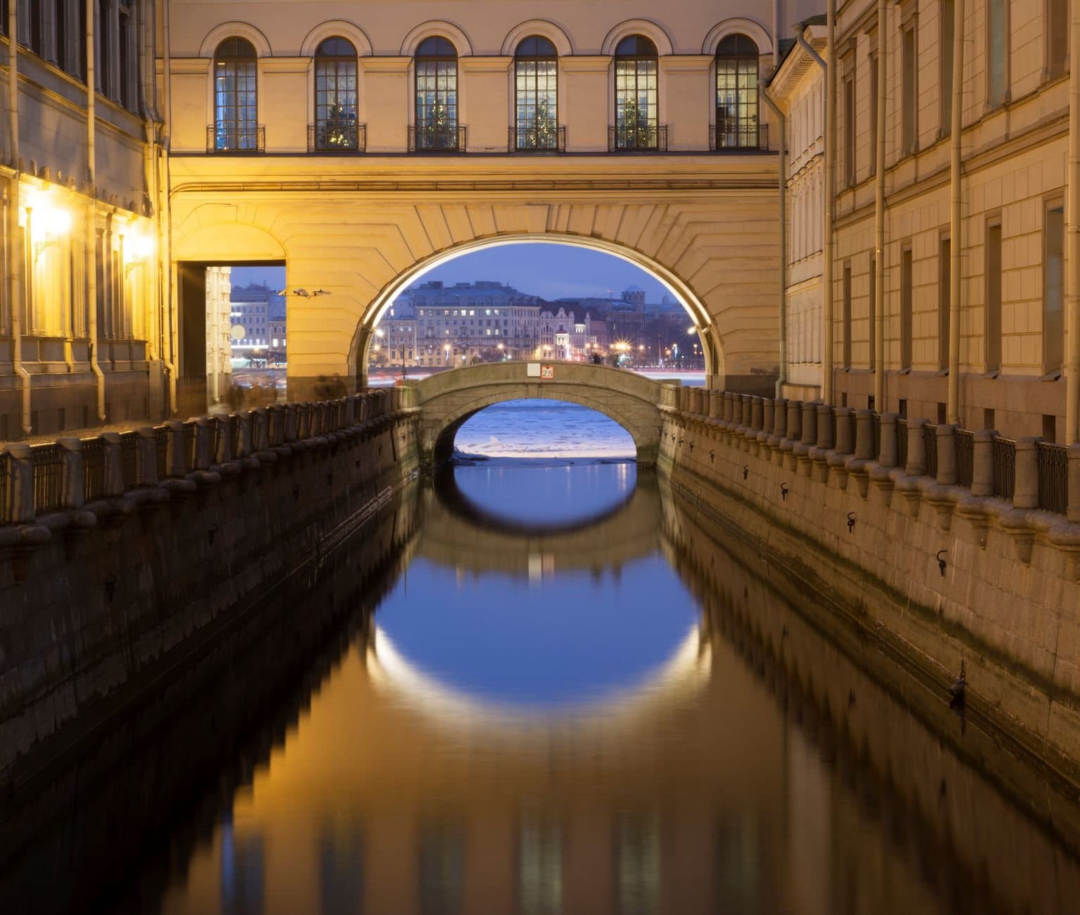 Beautiful view of a historic canal and bridge in Saint Petersburg at twilight, reflecting city lights.