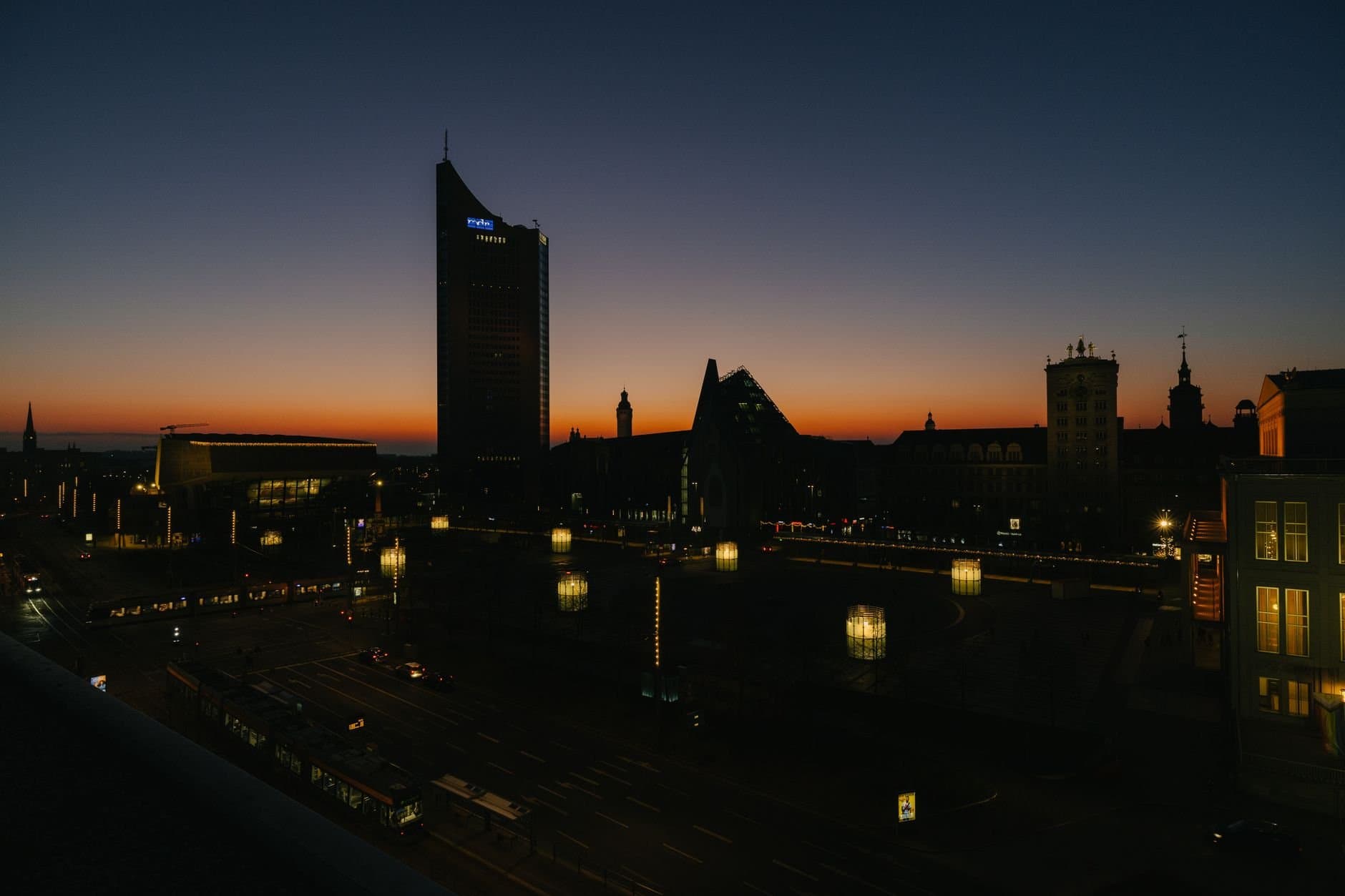 Dusk view of Leipzig's skyline with city lights and orange twilight sky.
