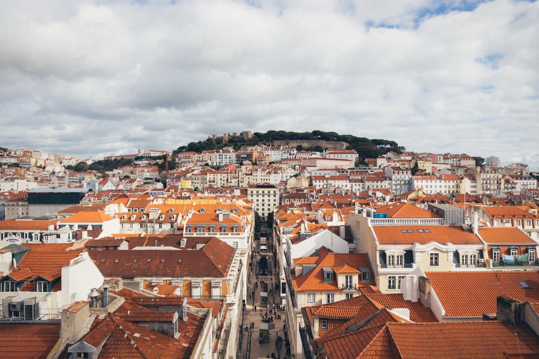 Aerial view of Lisbon's red rooftops and historic architecture under a cloudy sky.