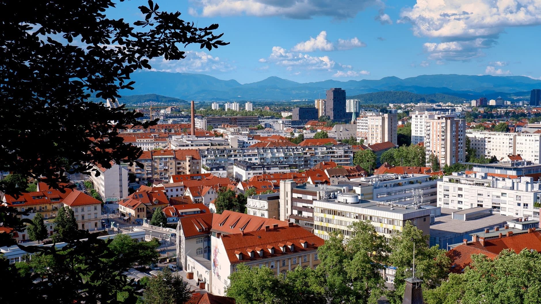 Breathtaking aerial view of Ljubljana cityscape featuring iconic red roofs, lush greenery, and distant mountains.