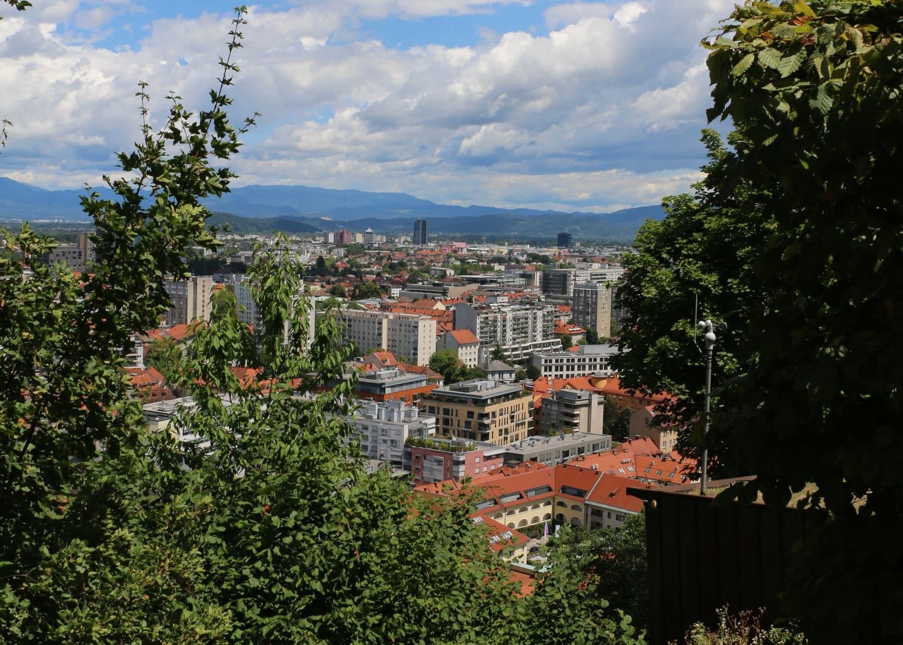 A vibrant cityscape of Ljubljana, Slovenia, framed by lush greenery and a clear sky.