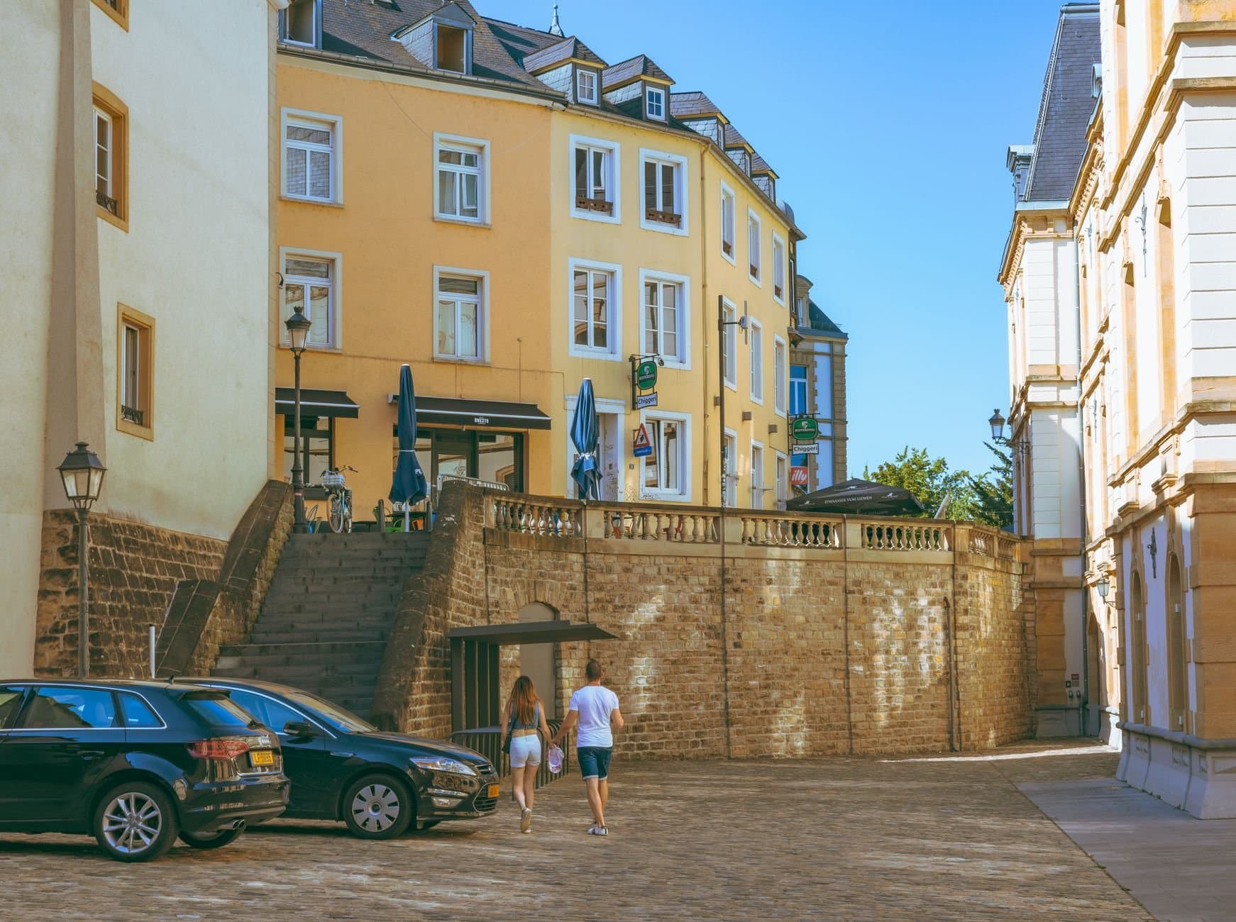 A couple walks along a picturesque street in Luxembourg City, showcasing historic architecture and urban charm.